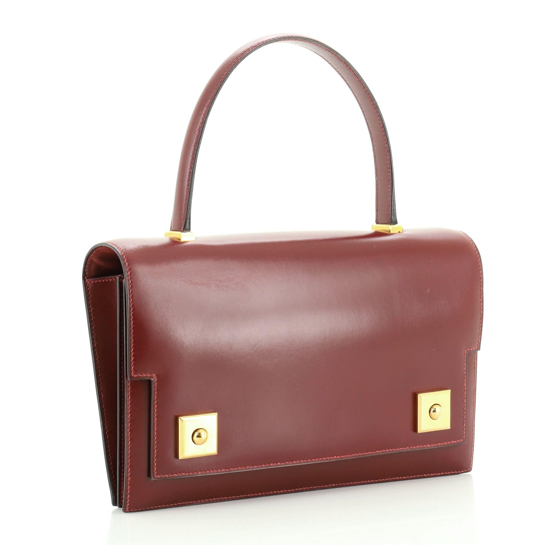 This Hermes Piano Handbag Box Calf, crafted from Rouge H red Box Calf leather, features a leather top handle, frontal flap, and gold hardware. Its magnetic peg-in-hole closures open to a Rouge H red Agneau leather interior with dual compartments,
