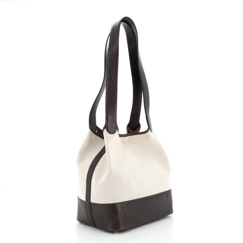 This Hermes Picotin Bag Toile and Leather GM crafted from Ecru neutral Toile H and Ebene brown Barenia leather, features dual looping leather handles and palladium hardware. It opens to an Ecru neutral Toile H and Ebene brown Barenia leather