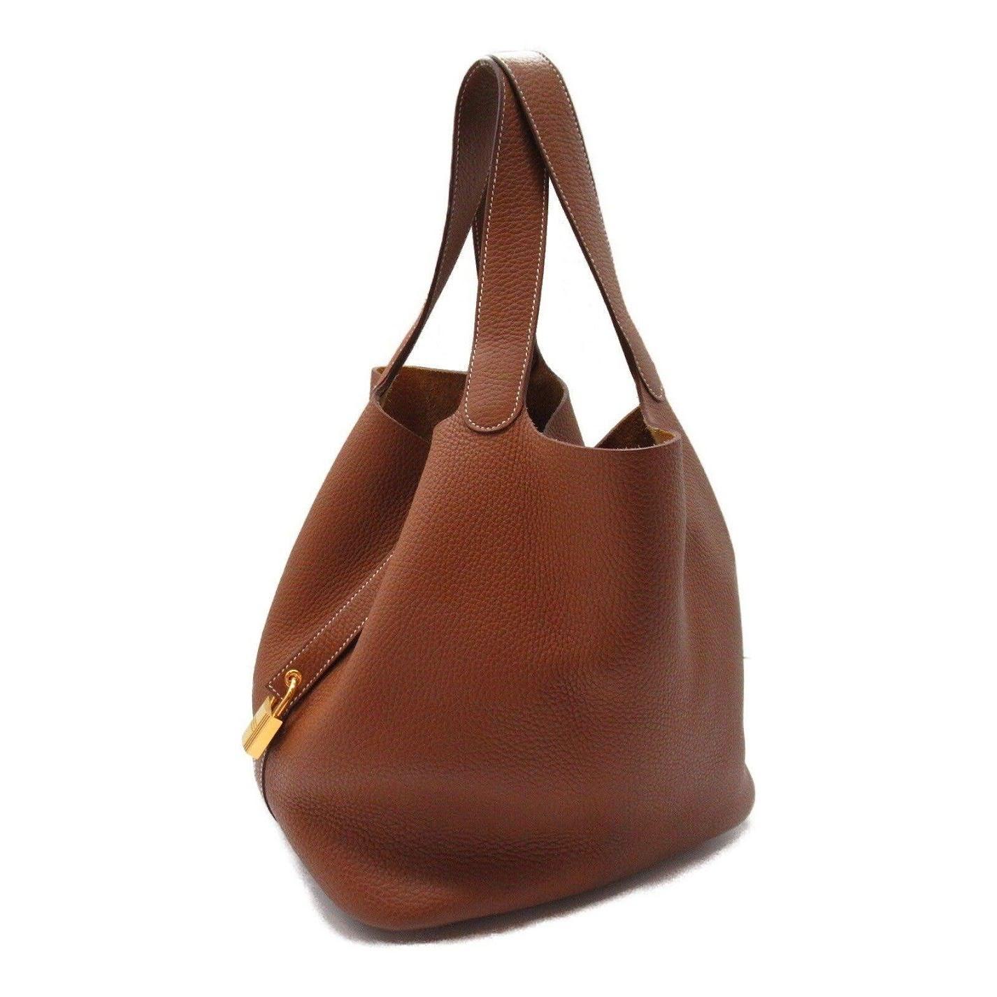Crafted of luxuriously soft Clemence calfskin leather in gold. This handbag features a unique one-piece reinforced design with leather top handles and a closure strap that a padlock can secure. This opens to a spacious suede interior. This is an