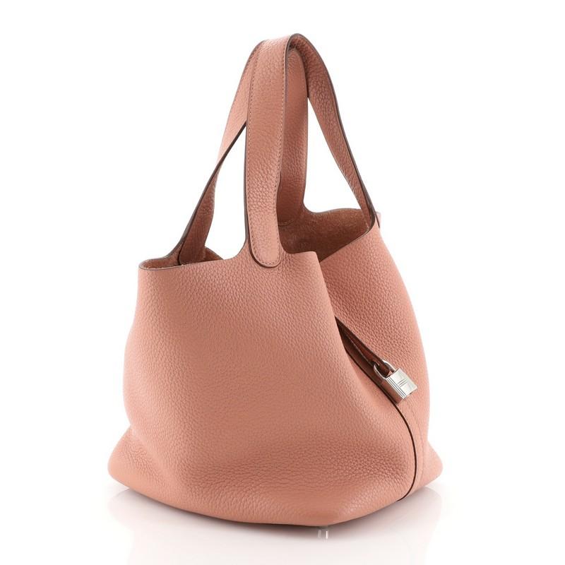 This Hermes Picotin Lock Bag Clemence PM, crafted from Rosy pink Clemence leather, features dual looping leather handles, a unique one-piece closing design with lock and secured by a belt strap, protective base studs and palladium-tone hardware. The