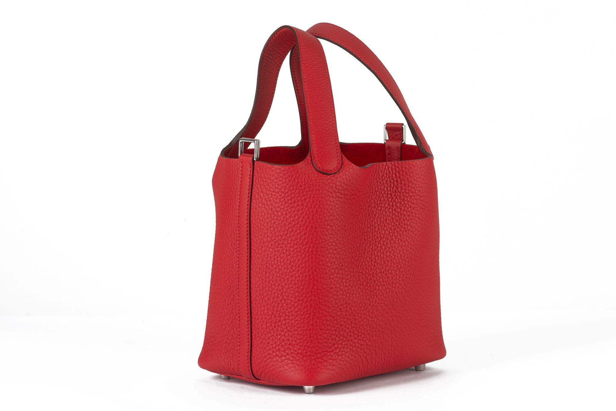 Questa tote di Hermès Picotin Lock è realizzata in pelle di vitello Clemence di colore rosso. Questa borsa è dotata di manici superiori in pelle e di una cinghia di chiusura che può essere fissata con un lucchetto dorato. Si apre su uno spazioso