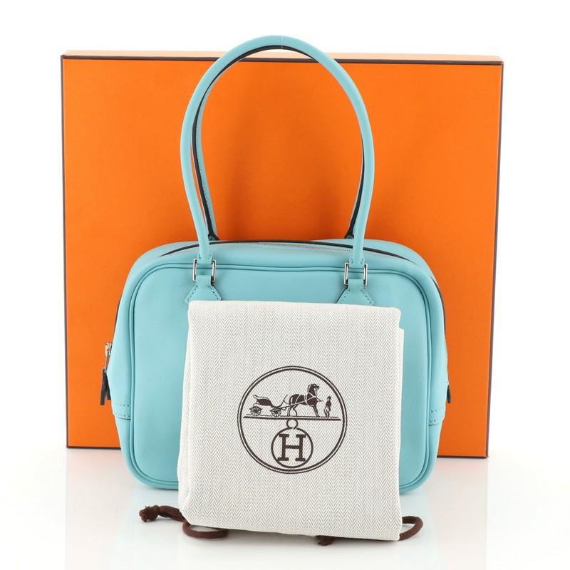 This Hermes Plume Bag Swift 21, crafted in Bleu Atoll blue Swift leather, features red dual rolled handles, protective base studs, and palladium hardware. Its zip closure opens to a Bleu Atoll blue Swift leather interior with slip pockets. Date