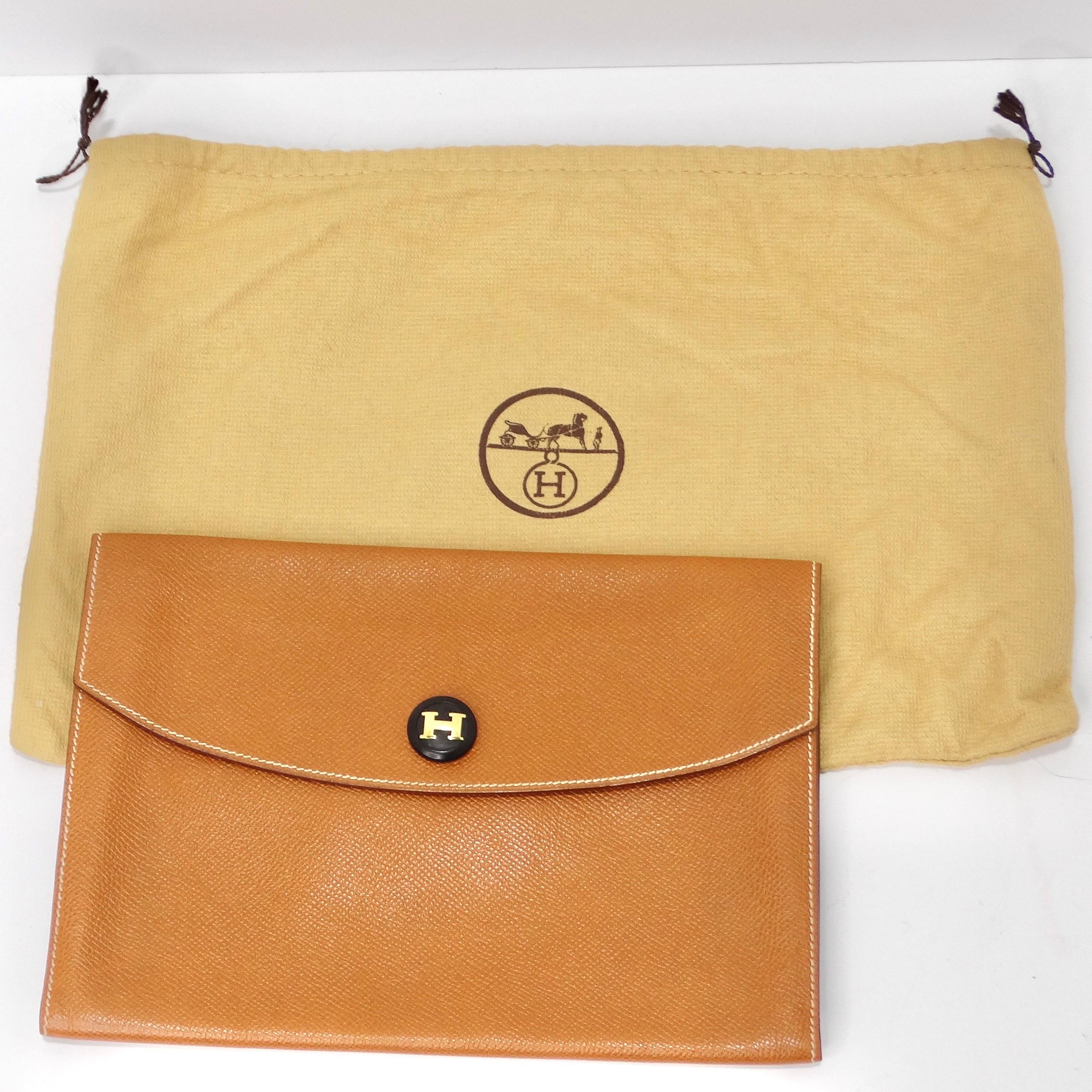 Introducing the epitome of timeless elegance - the Hermes Rio Envelope Pochette in a camel tone brown. This luxurious accessory features a chic snap-style closure and a striking black button at the center, adorned with a captivating gold-tone 'H'