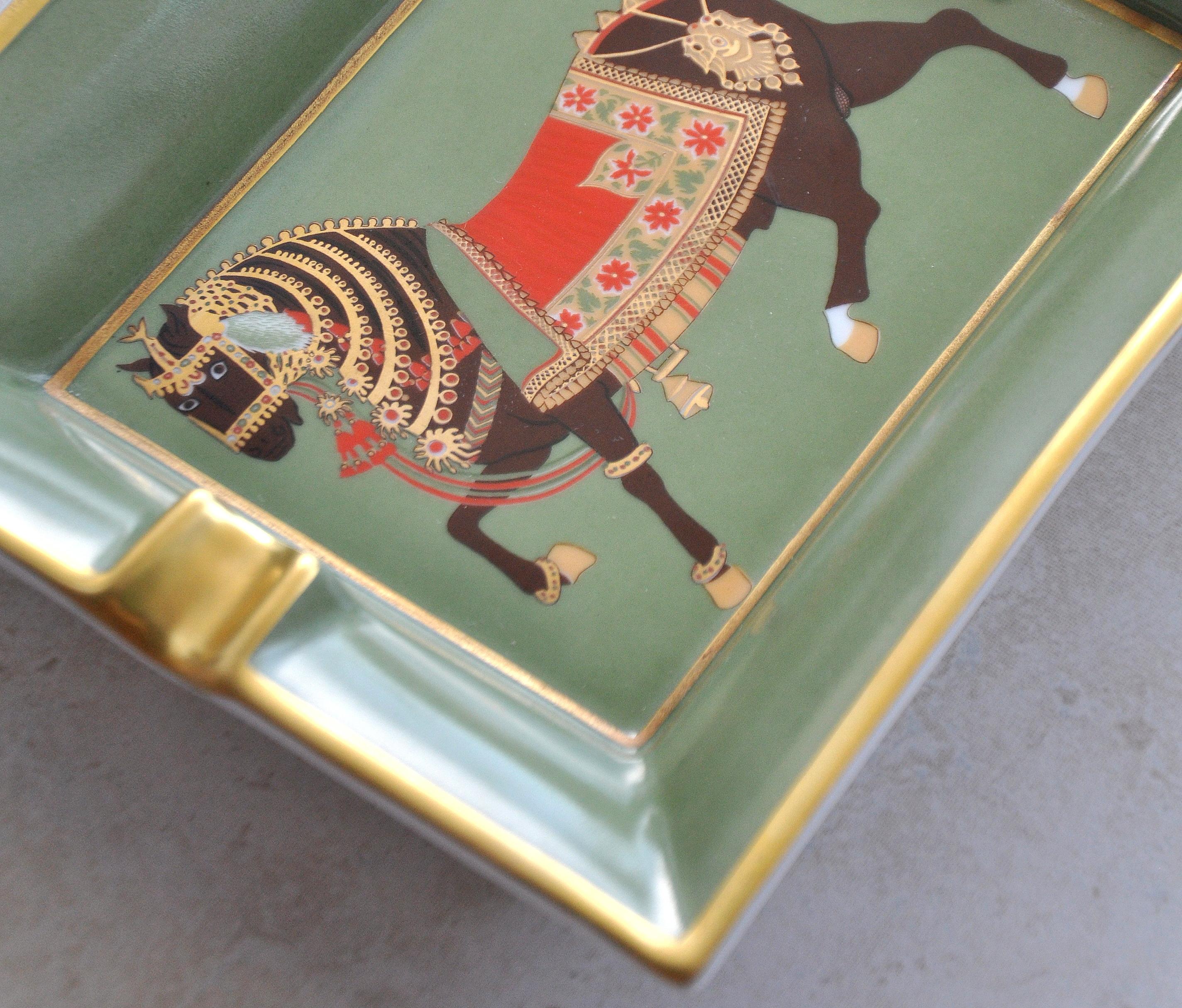 Fine French gilt porcelain cigar ashtray from the Hermès Cheval d'Apparat collection with Classic equestrian motif depicting an exquisitely detailed brown horse on a beautiful green background with abundant gilding, intricate details and suede on