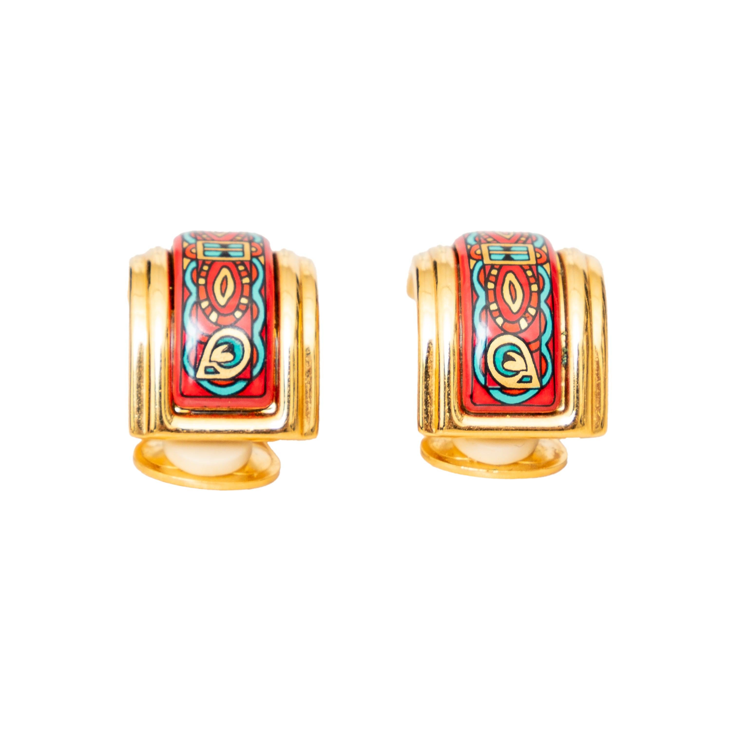 These stunning Hermès clip-on earrings feature gold-plated semi-hoops with a vibrant red and multicolored enamel inlay, adorned with intricate graphic details. A bold and stylish statement piece from Hermès.
 Inclusion: box. 
 Material: Gold-Plated