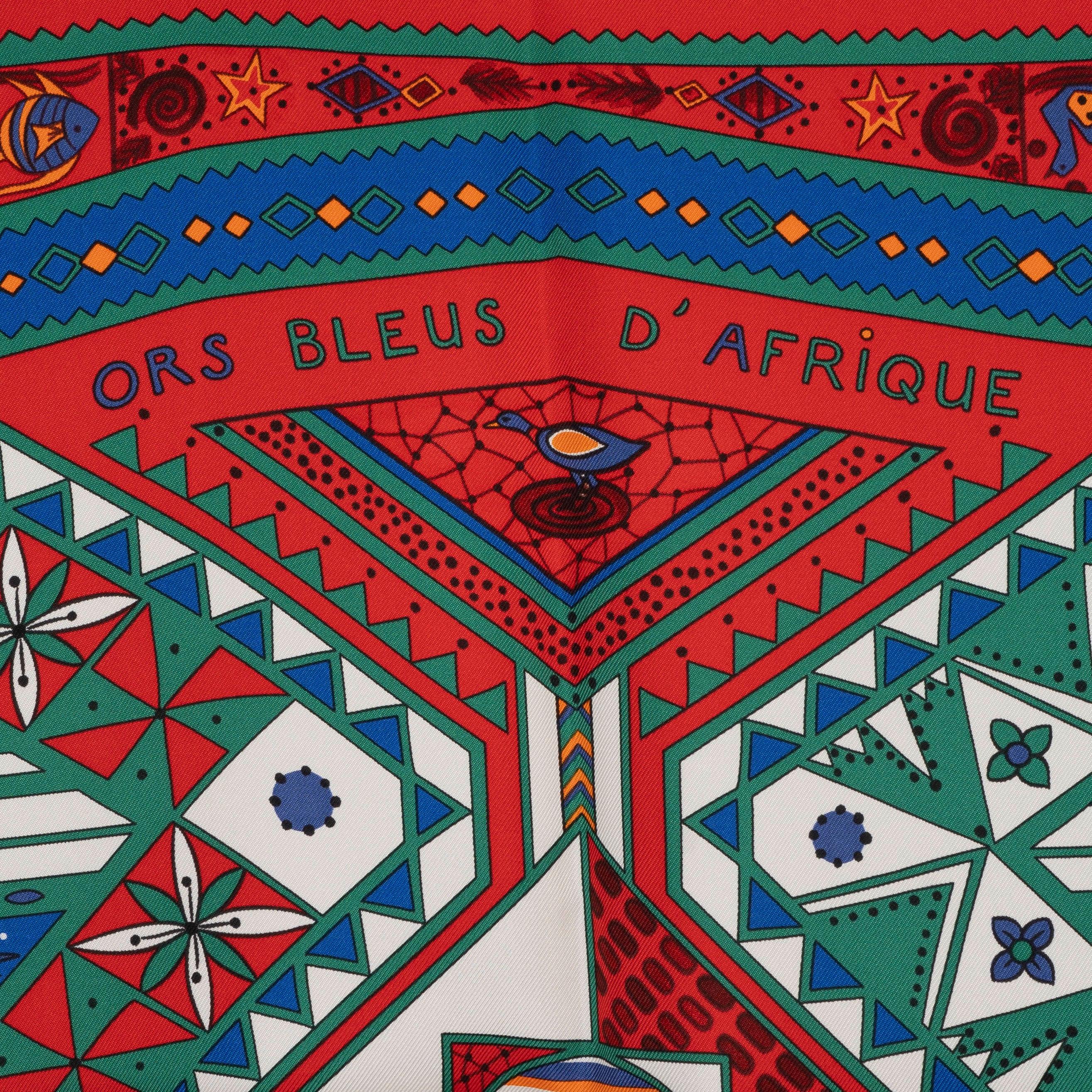 This 100% authentic Hermès Ors Bleus d'Afrique 90 scarf, designed by Zoé Pauwels, is crafted from luxurious red silk twill. It showcases a vibrant print featuring a variety of African animals depicted in blue, green, and white, celebrating the rich