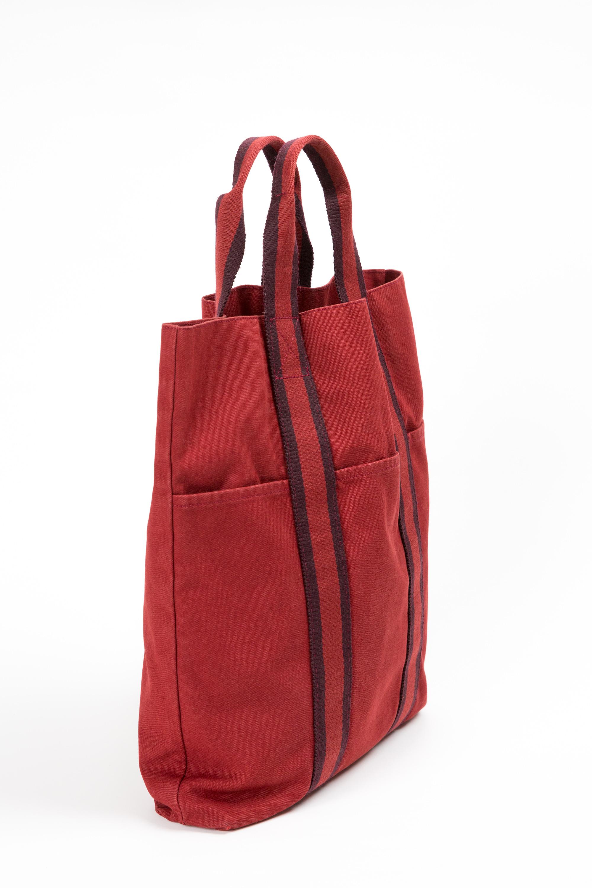 Hermes red canvas “Toto” long tote bag featuring bicolor handles, front pockets, inside pocket.  
Circa 1990s 100%cotton
In good vintage condition . Made in France. 
Length: 13.4in. (34cm)
Height: 14.5in. (37cm)
Width: 2.3in. (6cm)
We guarantee you