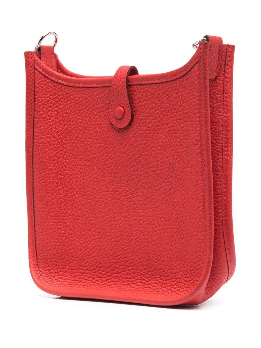 Crafted in a classic shade of red, in Togo leather and Palladium hardware, this red TPM Evelyne bag by Hermès remains stylish, functional and contemporary in a refined saddle-like shape with a perforated H logo decorating the front. The bag displays