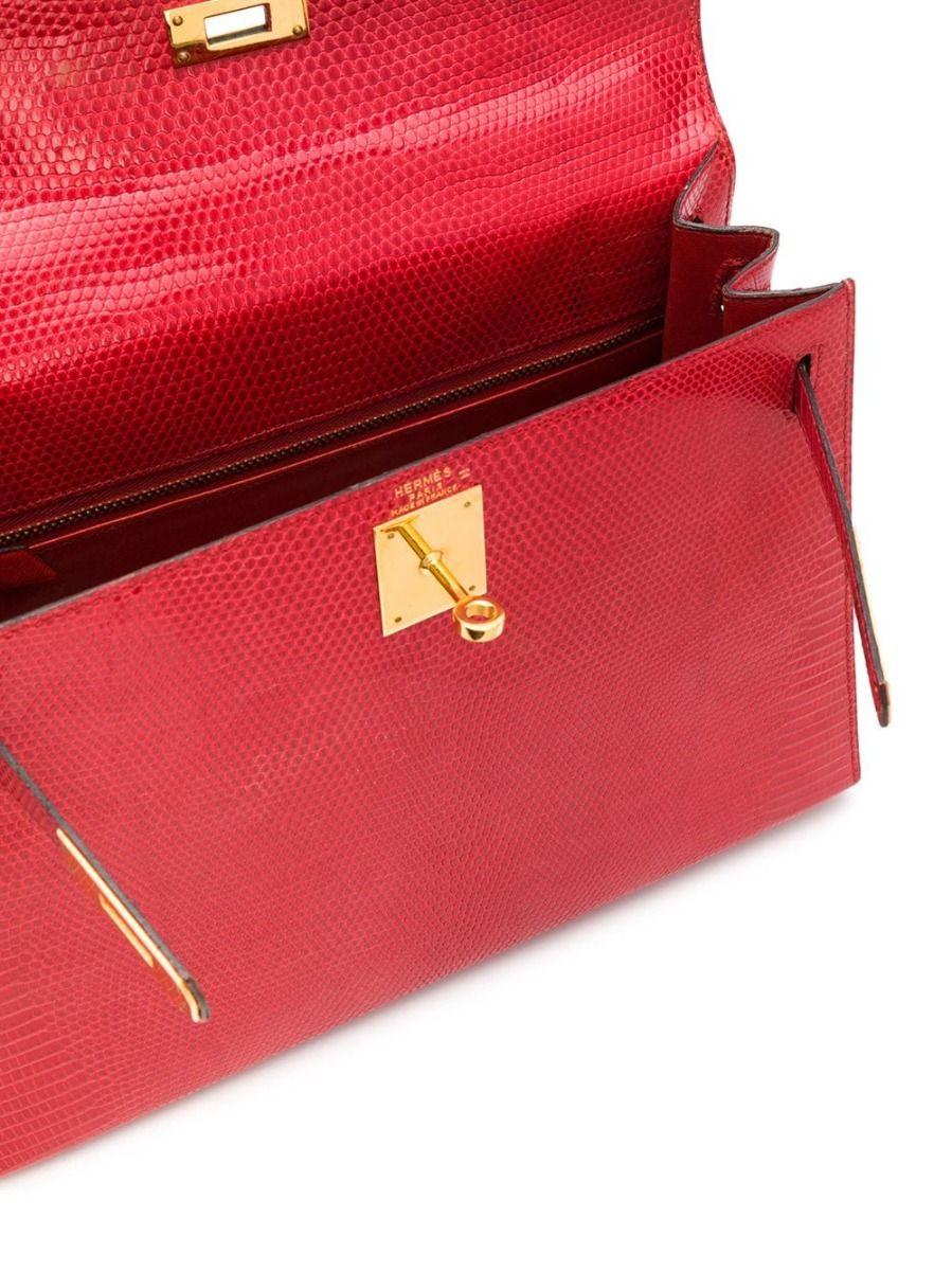 Crafted in France from lizard leather, a rare exotic Hermès skin known for its small scales and noticeably glossy finish. this structured, vintage bag features rigid corners and matching stitching with concealed piping. Featuring a vivid red