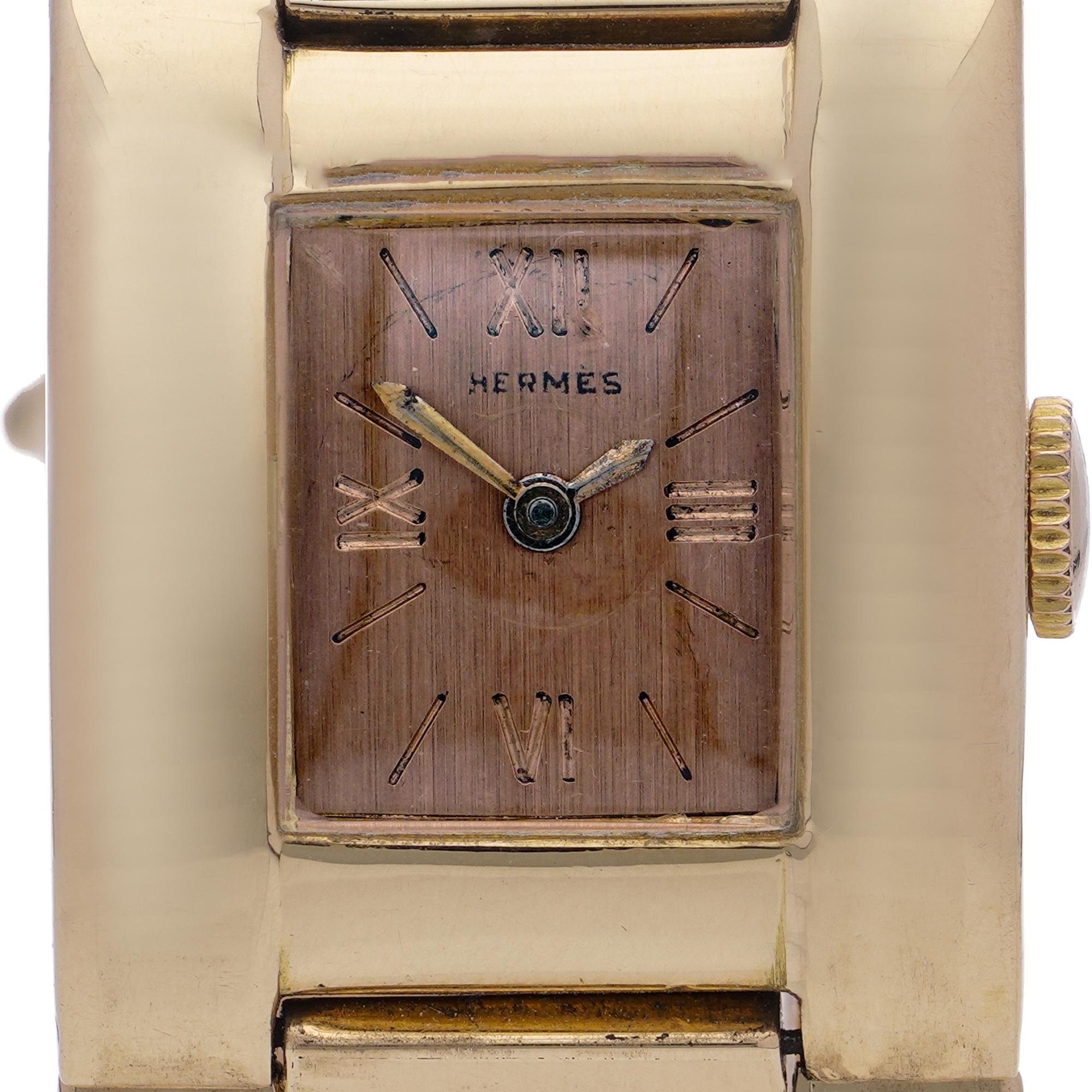 Eine stilvolle und elegante Damenarmbanduhr von Hermès aus der Mitte des Jahrhunderts, komplett aus 18 Karat Gelbgold gefertigt. Mit ihrem rechteckigen Gehäuse mit weichen Konturen und einem roségoldfarbenen Zifferblatt verkörpert sie die klaren,