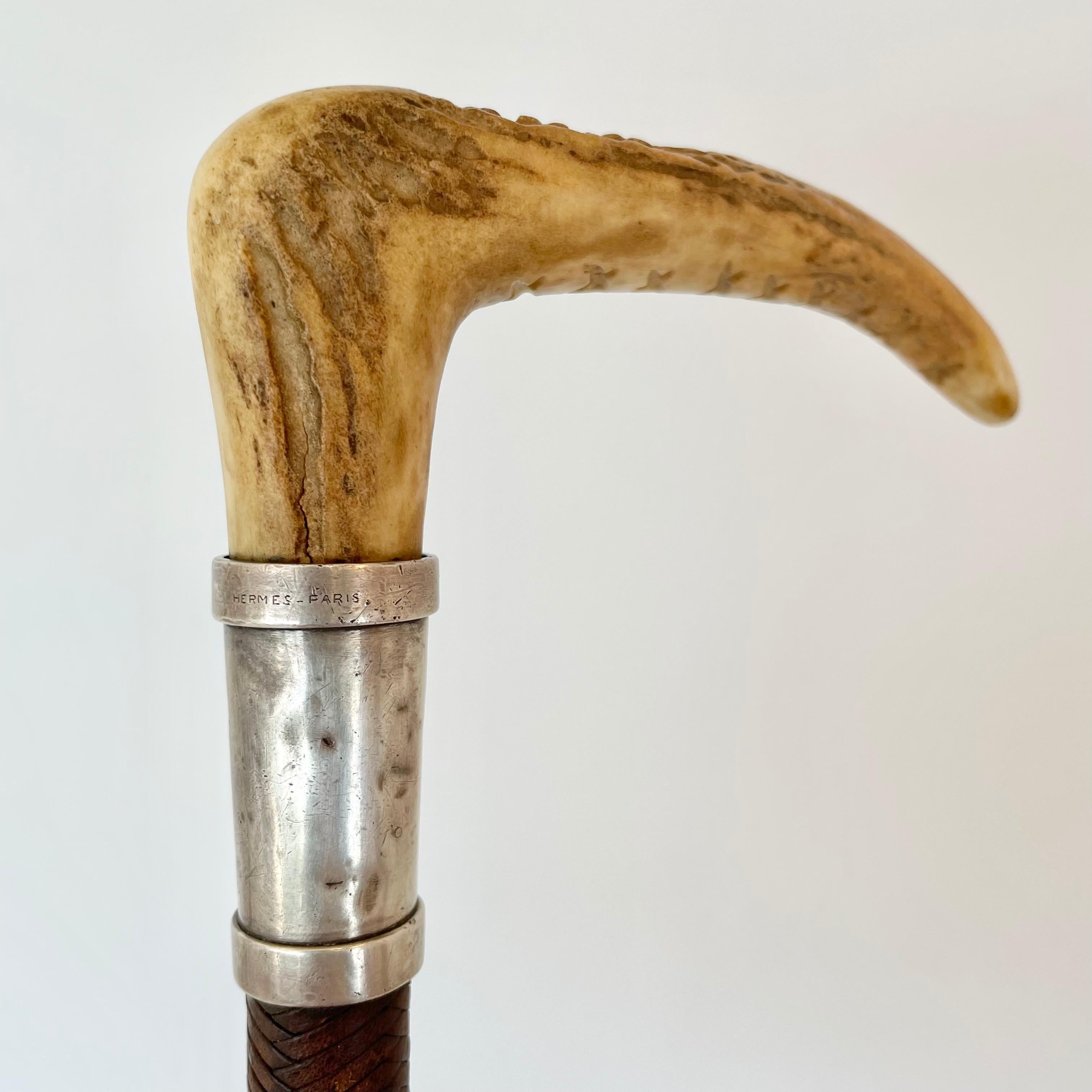 Vintage Hermes riding crop with deer antler handle. The shaft is covered in a beautifully braided leather and finished at the bottom with twine. The stag antler is fastened at the top with a silver plated collar bearing the Hermes Paris engravings