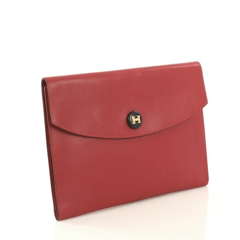 This Hermes Rio Clutch Leather PM, crafted from Rouge Vif red Box Calf leather, features logo embellished snap button and gold hardware. Its snap button closure opens to a Rouge Vif red Box Calf leather interior. Date stamp reads: V Circle (1992).