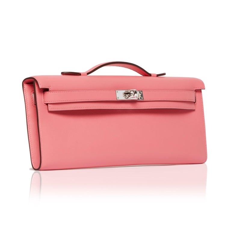 A sought after piece, this supple swift leather 2021 Rose Azalee Kelly Cut Clutch bag from Hermès features tonal stitching, front straps and a top flat handle. The toggle closure is accented by silver-tone palladium hardware and opens to reveal an