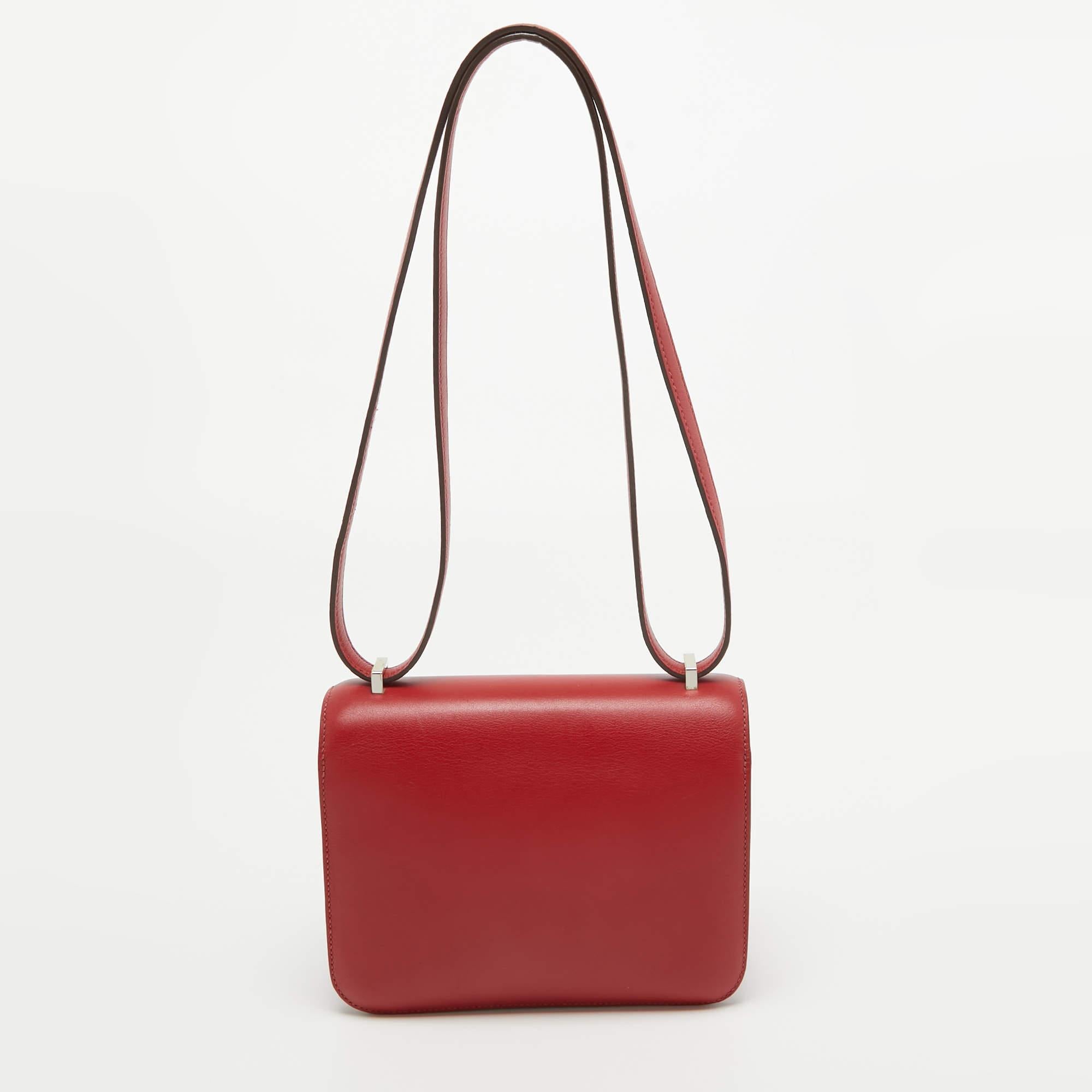 This Hermes Rouge Casaque Constance 18 Mini is crafted using Swift leather and features the iconic H clasp on the front flap. The shoulder strap lets you carry it gracefully, and the fine finish of the sturdy silhouette projects a luxe look. Get