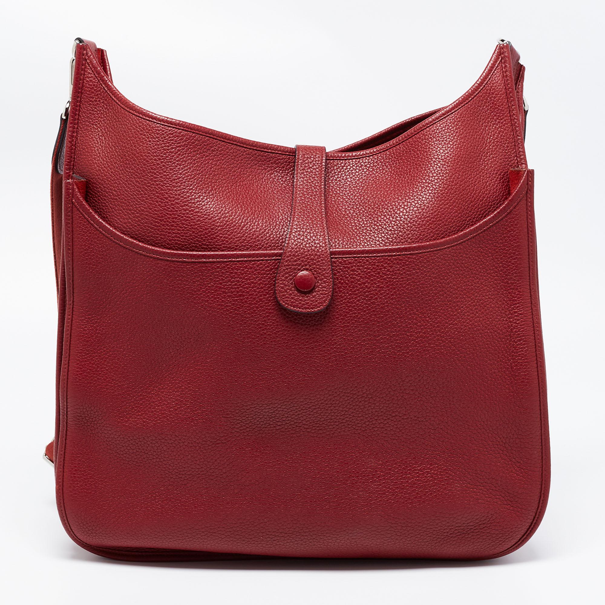 This Evelyne III TGM bag from the House of Hermes exudes the right amount of class and elegance. Crafted from Rouge Garance Togo leather, this bag is adorned with a shoulder strap and silver-tone hardware. It accommodates an unlined interior. Make