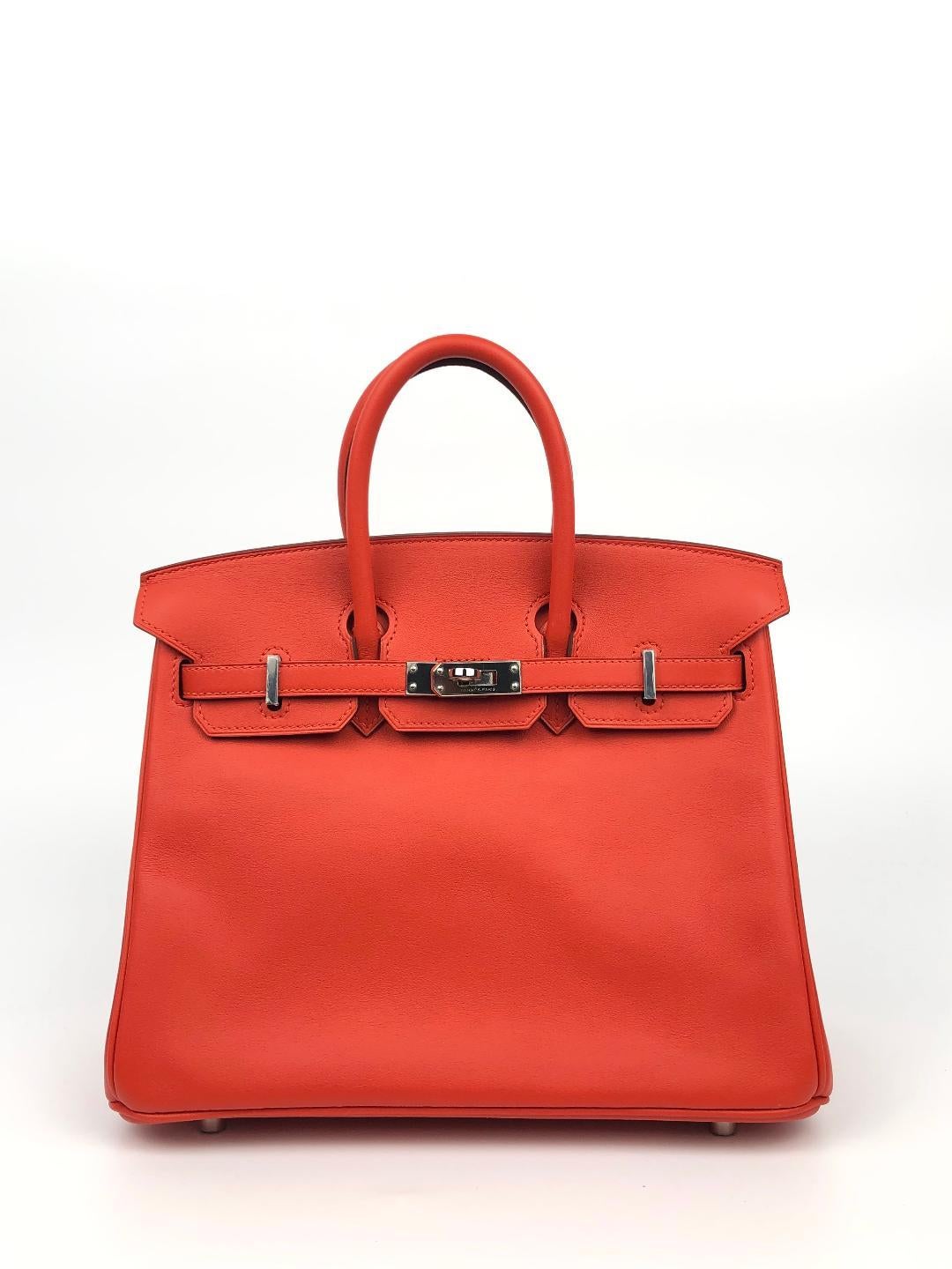 This authentic Hermès Rouge Tomate Swift Leather 25 cm Birkin Bag is in pristine unworn condition with plastic intact on the hardware.

Waitlists exceeding a year are commonplace for the intensely coveted classic leather Birkin bag.  Each piece is