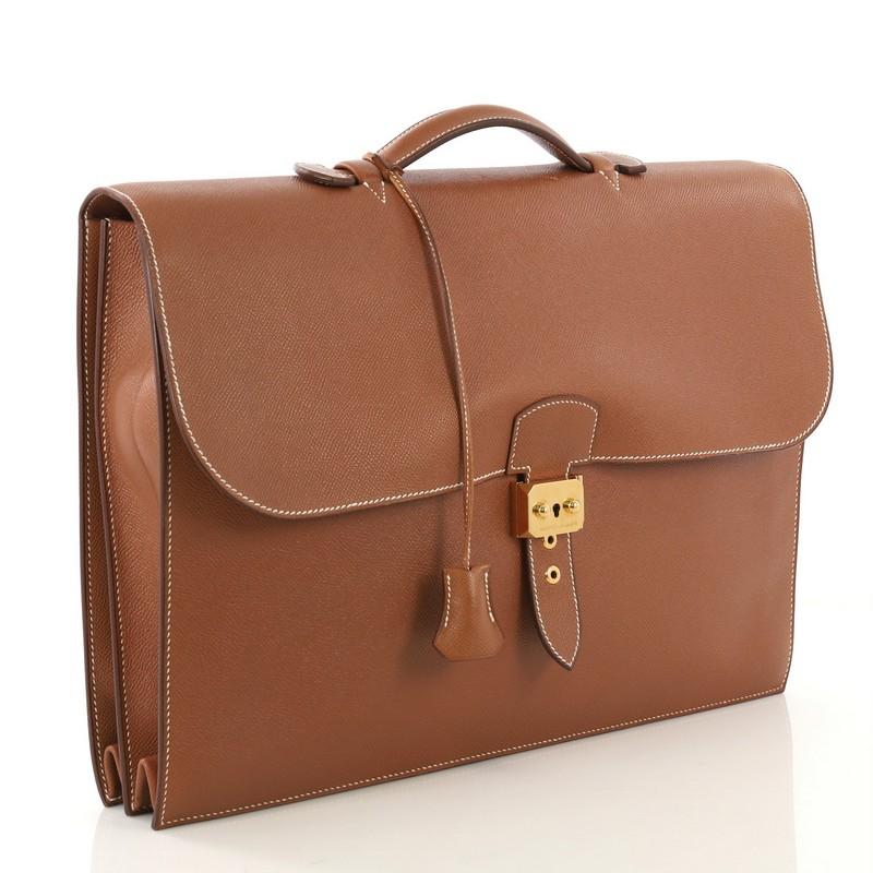 This Hermes Sac a Depeches Bag Courchevel 41, crafted from Gold brown Courchevel leather, features flat top handle, accordion side gussets, and gold hardware. Its flip lock closure opens to a Gold brown raw leather interior with two main