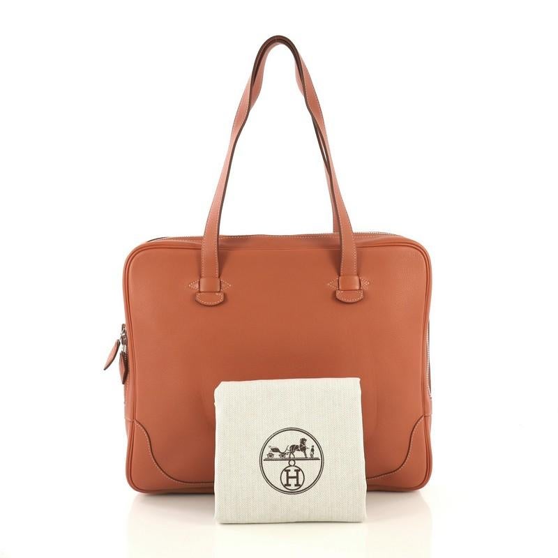 This Hermes Sac Trimset Bag Leather, crafted from Flamingo orange Evercolor leather, features dual flat handles and palladium hardware. Its zip closure opens to an Ecru neutral Toile Chevron interior with a middle zip compartment and side slip