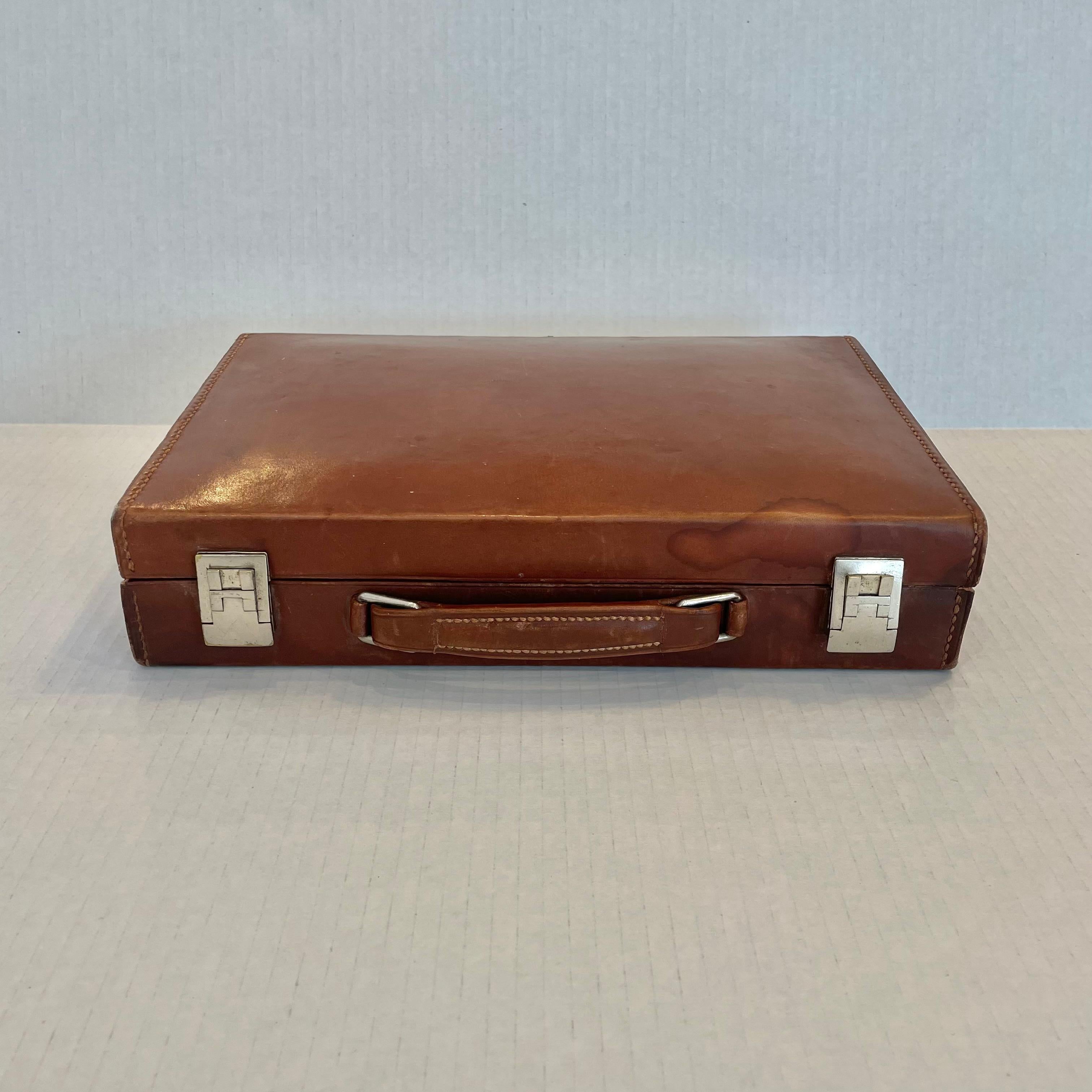 Handsome saddle leather case by French fashion house, Hermes. Made in the 1950s. H metal buckles flank each side of the case. Case opens up to reveal 'HERMES - MADE IN PARIS' on leather. Inside there is a large grouping of shaving/toiletry items.
