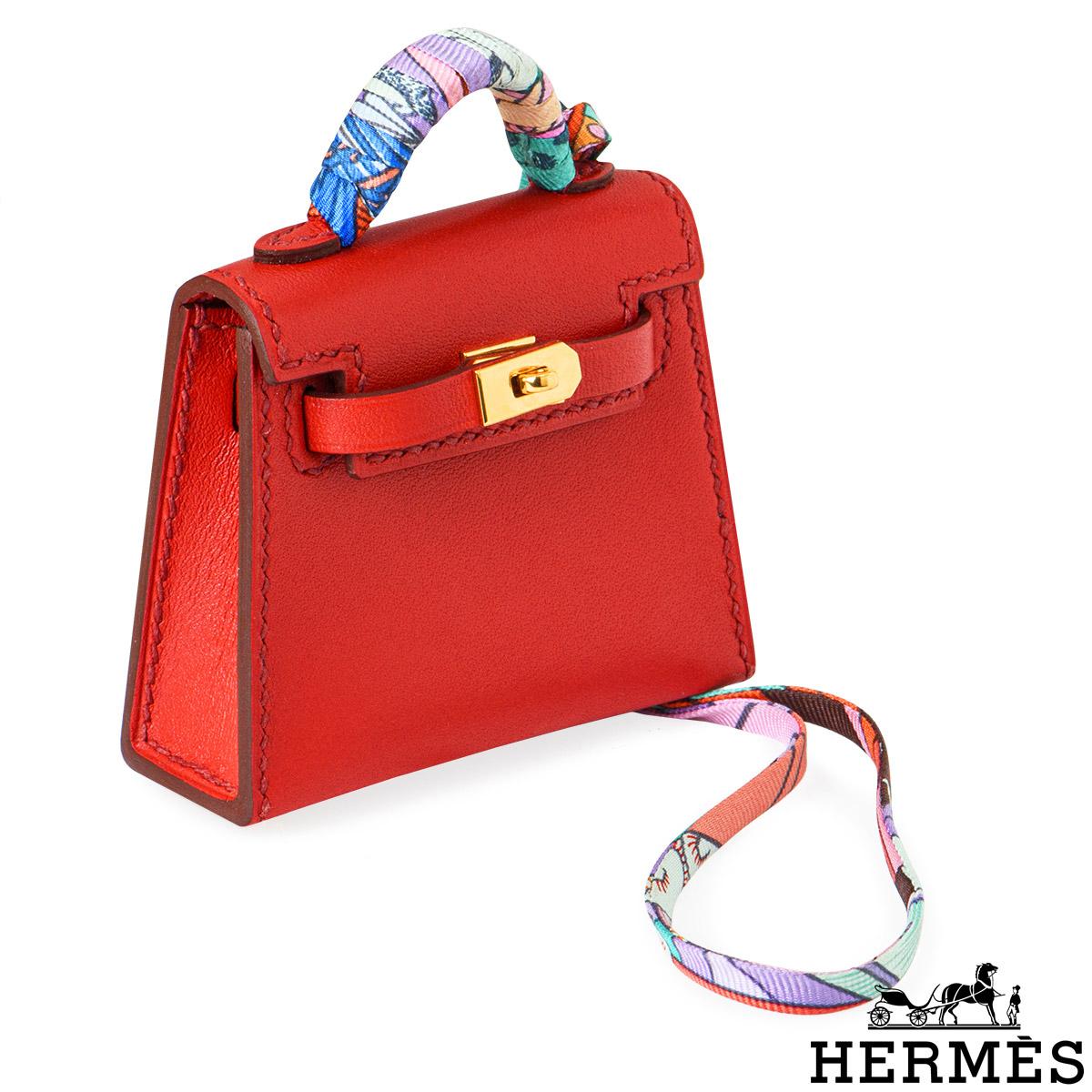 A charming accessory - an adorable Hermès Mini Kelly Twilly bag charm. The exterior of this Kelly bag charm features a Sanguine Tadelakt leather detailed with tonal stitching. It features gold-tone hardware with a front toggle closure, and a top