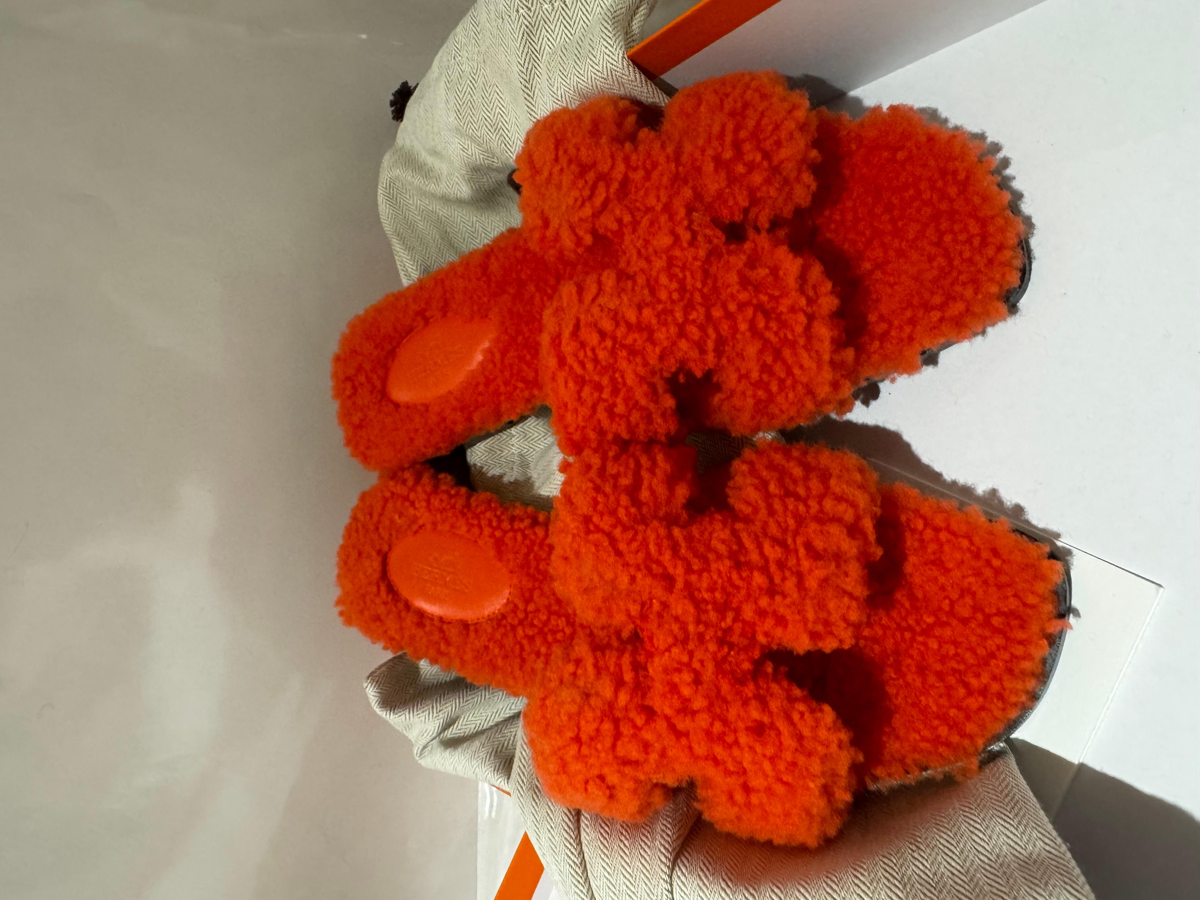 I sandali Hermes Oran sono in shearling arancione e presentano l'iconico cinturino incrociato H. H. con una suola in gomma nera. Taglia 37, con dustbag e scatola. 