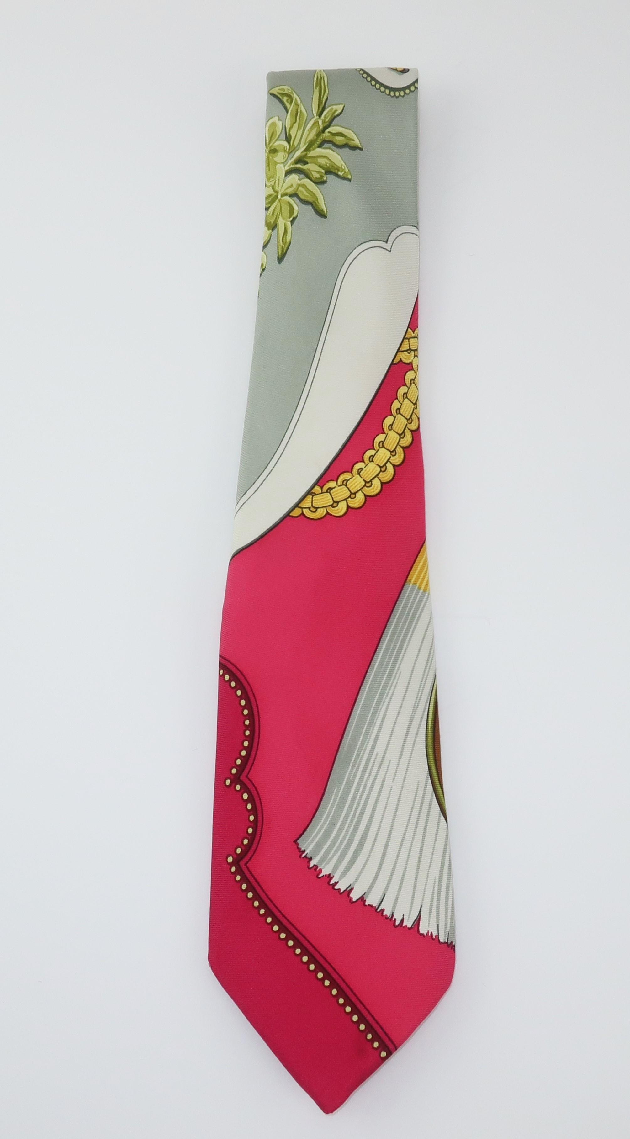 A vintage Hermes menswear French silk necktie with a trompe l'oeil design featuring tassels, chains and medallions along with a little flora and fauna all in shades of raspberry red, light gray, pearly white, golden yellow and greens. It is