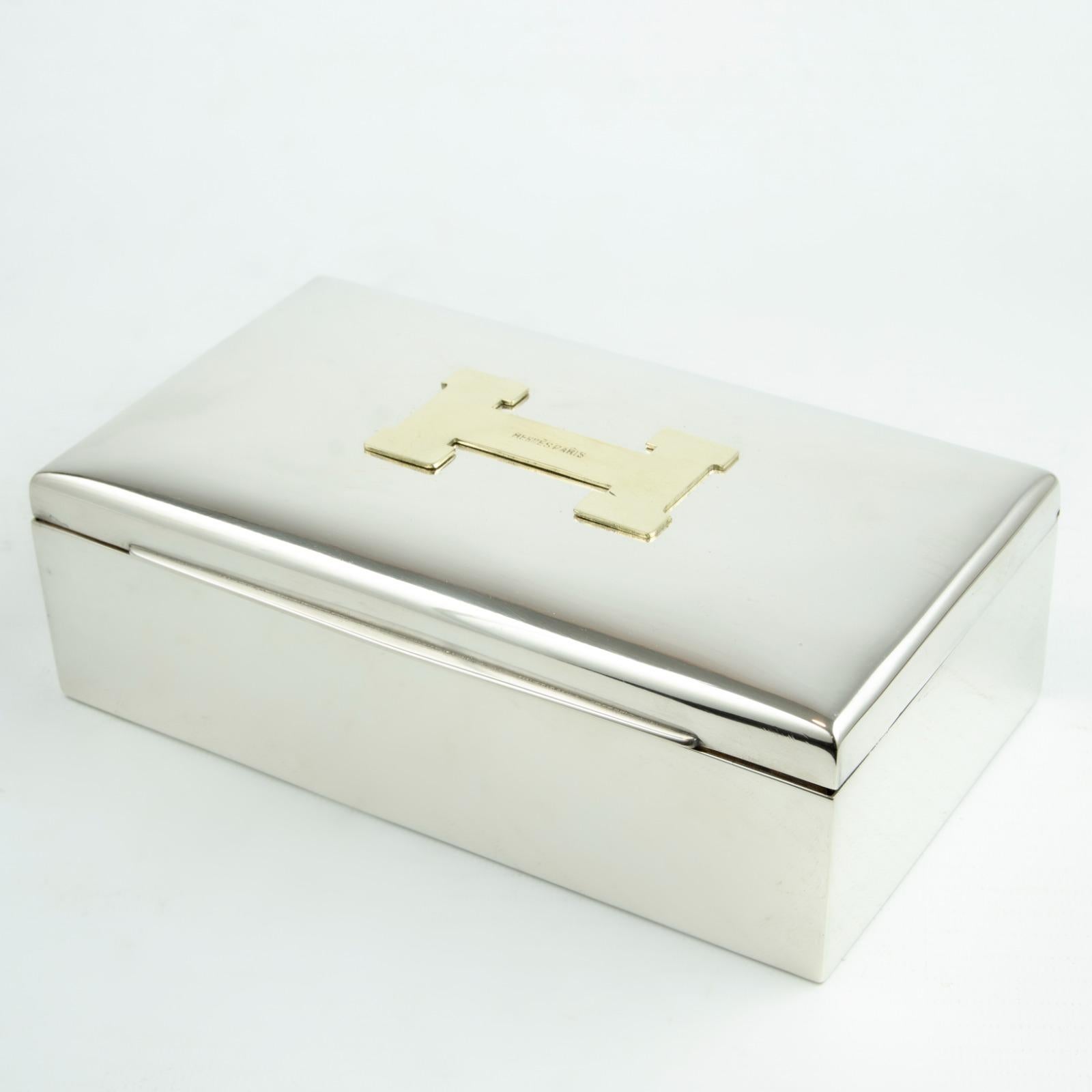 HERMES Paris vintage rare silver tone metal box featuring a large gold plated H design on top.

Material : Silver tone metal hardware / Gold tone metal hardware / Wood panel inner compartment.

Measurements
10,3 centimeters Depth
18,5 centimeters