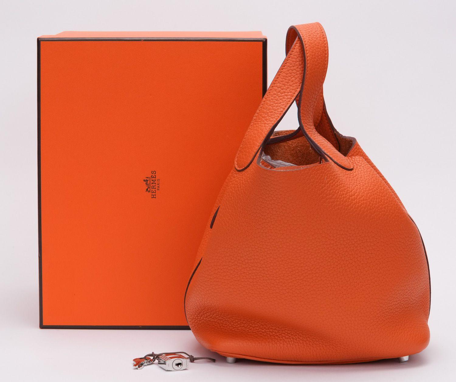 Picotin Lock handbag from Hermès Pre-Owned featuring orange, Taurillon Clemence leather, two flat top handles, lock and metal feet. It's in excellent condition nearly perfect. The handles drop is 6' and the bag comes with the original box and