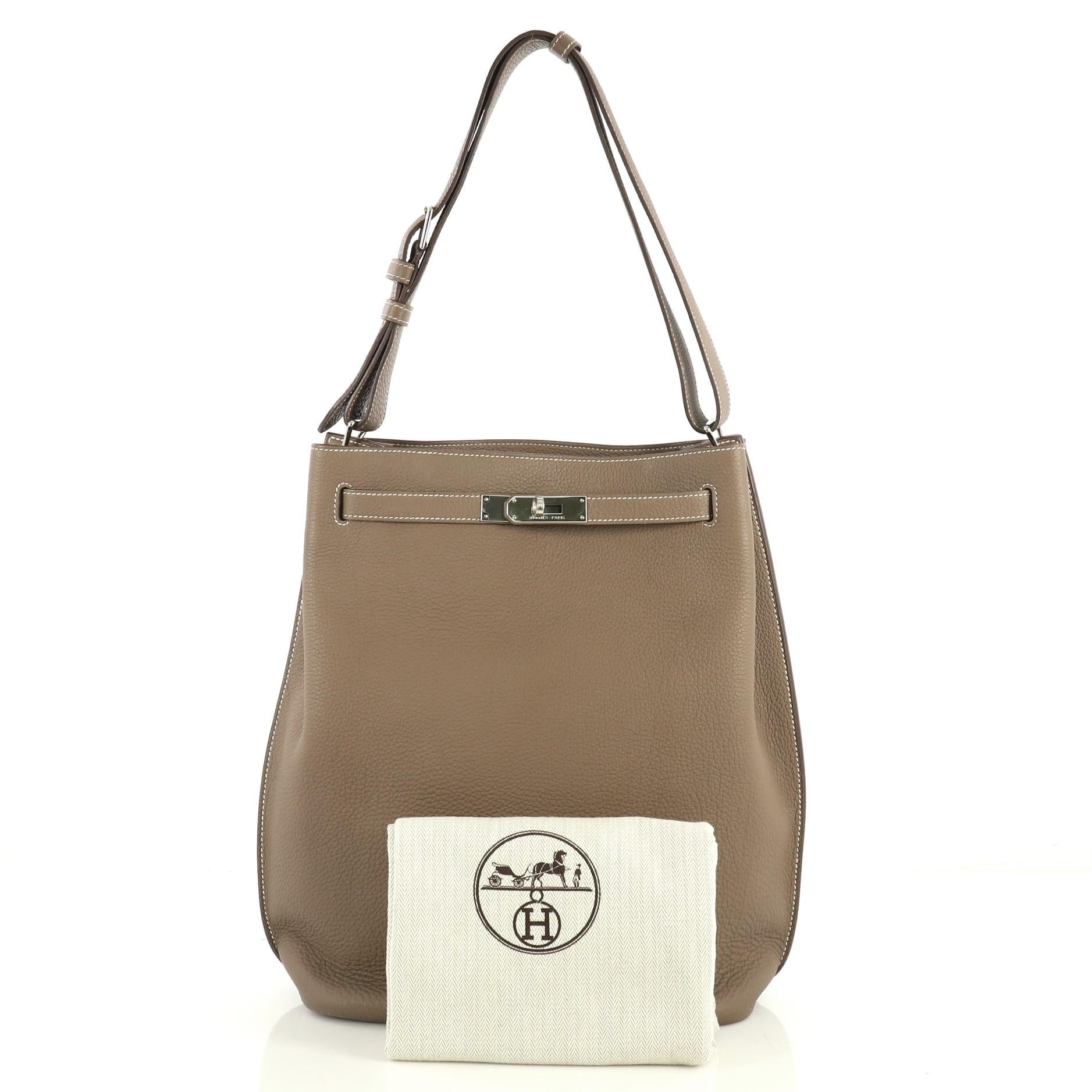 This Hermes So Kelly Handbag Togo 26, crafted in Etoupe neutral Togo leather, features an adjustable strap and palladium hardware. Its turn-lock closure opens to an Etoupe neutral Chevre leather interior with side zip and slip pockets. Date stamp