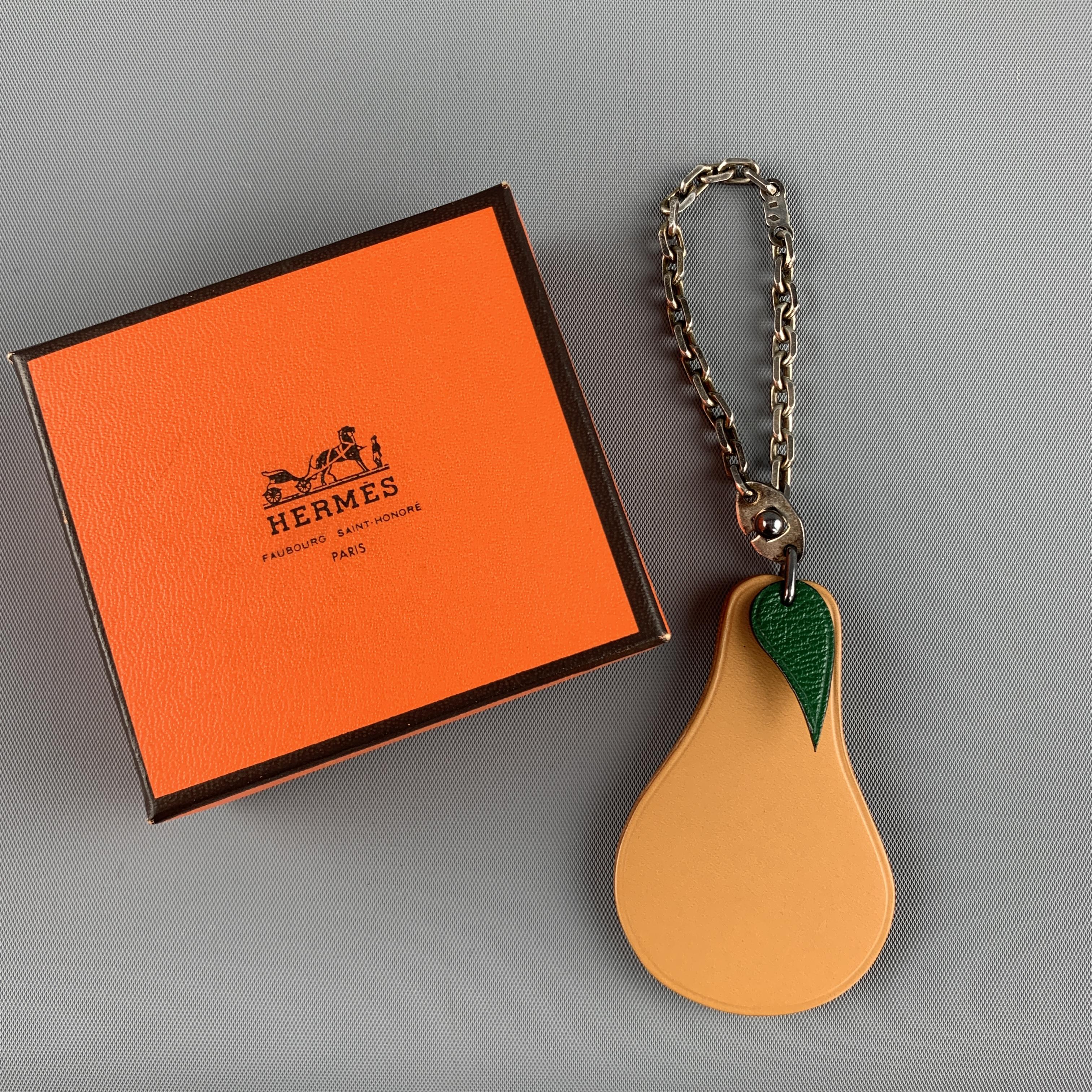 HERMES bag charm features a tan pear shaped leather charm with a green leather leaf on a sterling silver chain. Aging on metal. As-is. With box. Made in France.

Very Good Pre-Owned Condition.
Marked: 925

Charm: 6 x 4 cm.
Chain Drop: 6 cm.