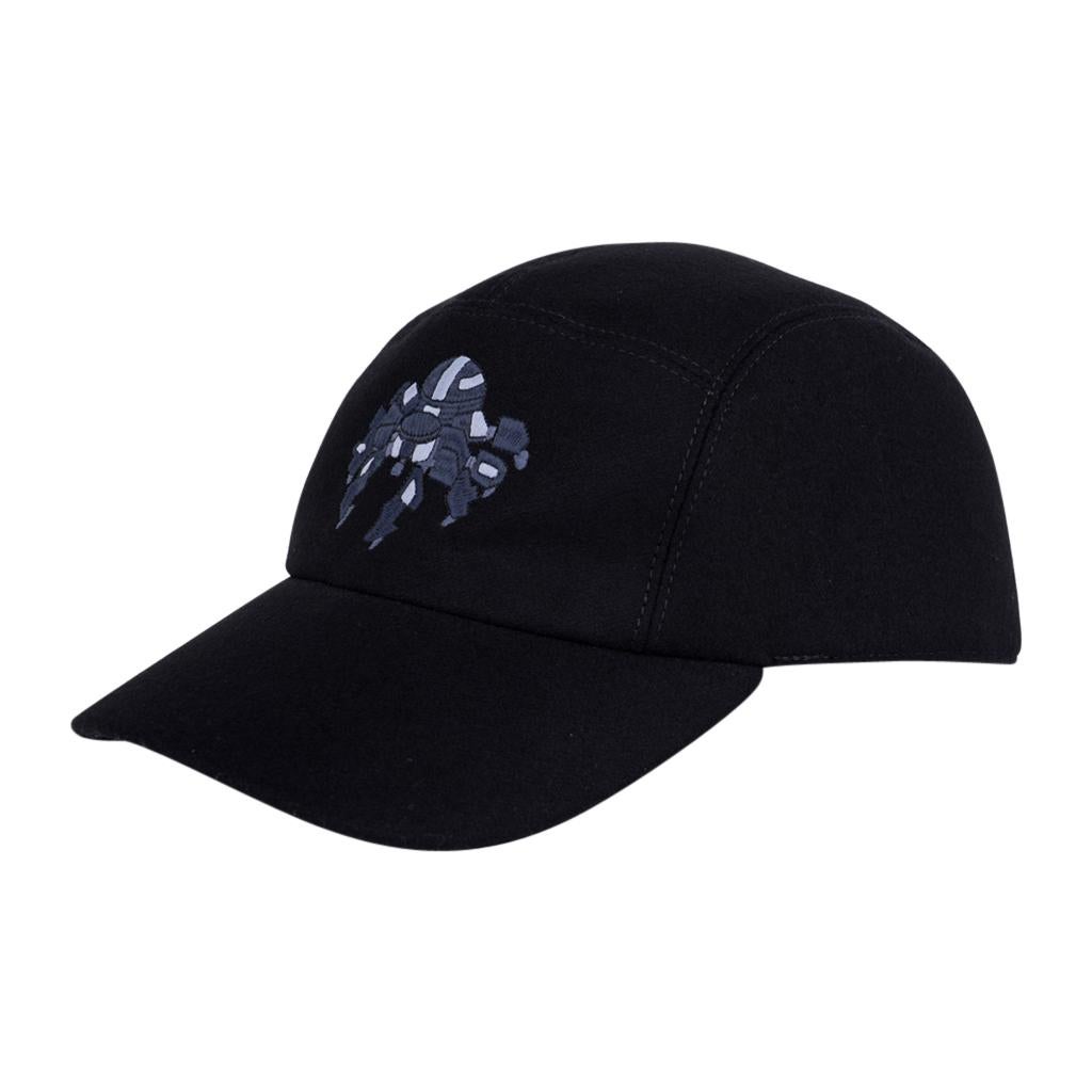 Mightychic offers a limited edition Hermes Black cashmere Spider Robot cap.  
The cap shows a blue and gray embroidered robotic spider across the front center.
2 Hermes Paris Clou de Selle snaps at rear. 
Identical caps under separate listing in