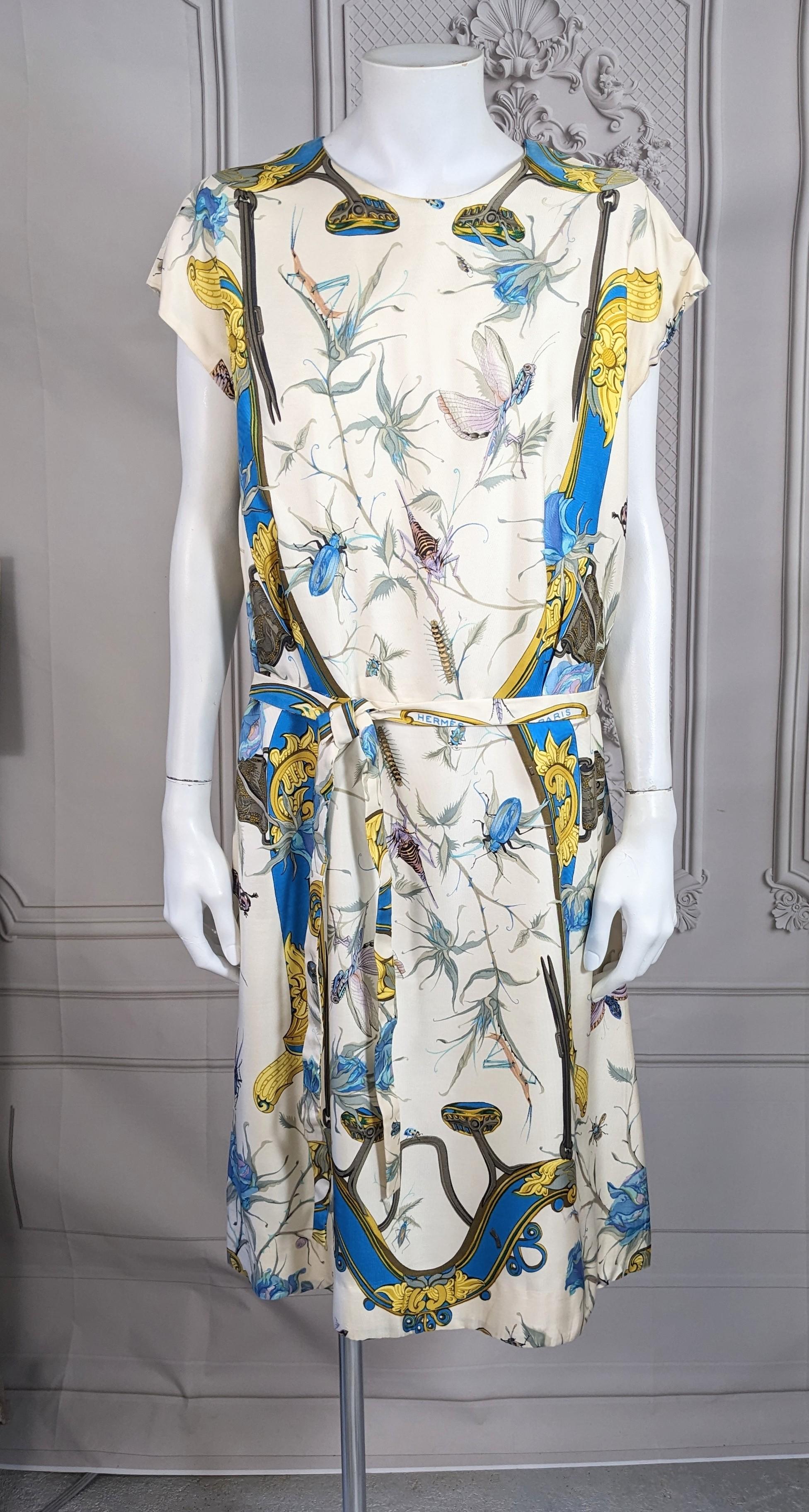 Hermes Sport Ivory silk twill afternoon dress printed with various insects and foliage, within an equestrian unfurling border of gold and blue decorative straps. Self belt signed Hermes in the print,  2 side zippers for entry.  Good Condition,