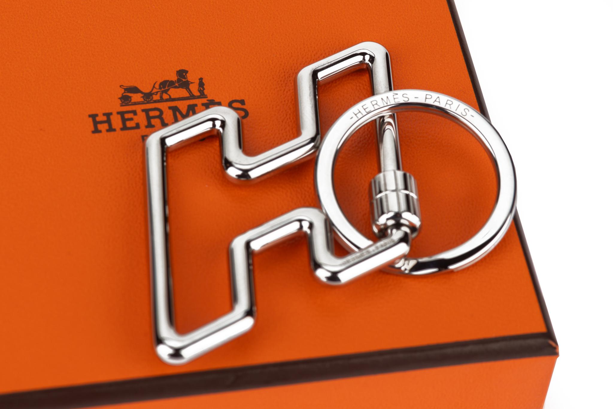 The Hermès H - Too Speedy Key ring in metal with brushed stainless steel hardware. Too Speed reproduces the design in movement of the H Speed belt. Comes with ribbon, original dustcover and box. Brand new in unused condition.
