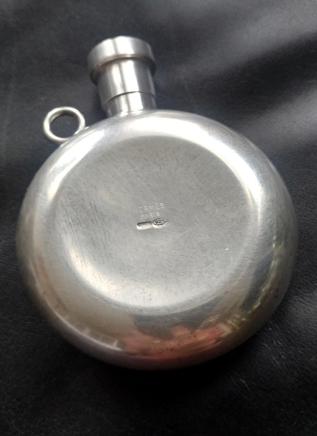 An elegant petit perfume flask pendant necklace.
Removable red leather strap.
Sterling silver marked 925.
Engraved on bottom “Montre Nomade Hermes Bale 2001“
Original box included.