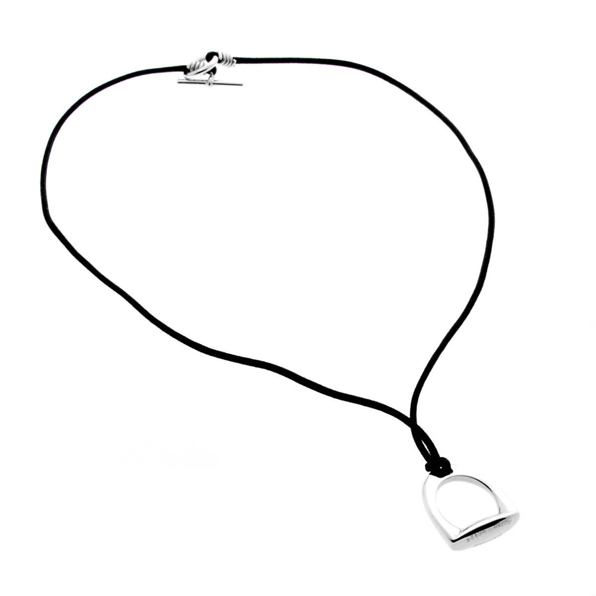 A chic Hermes necklace featuring a solid Stirrup motif crafted in 18k white gold, the pendant is suspended on a black woven string necklace.