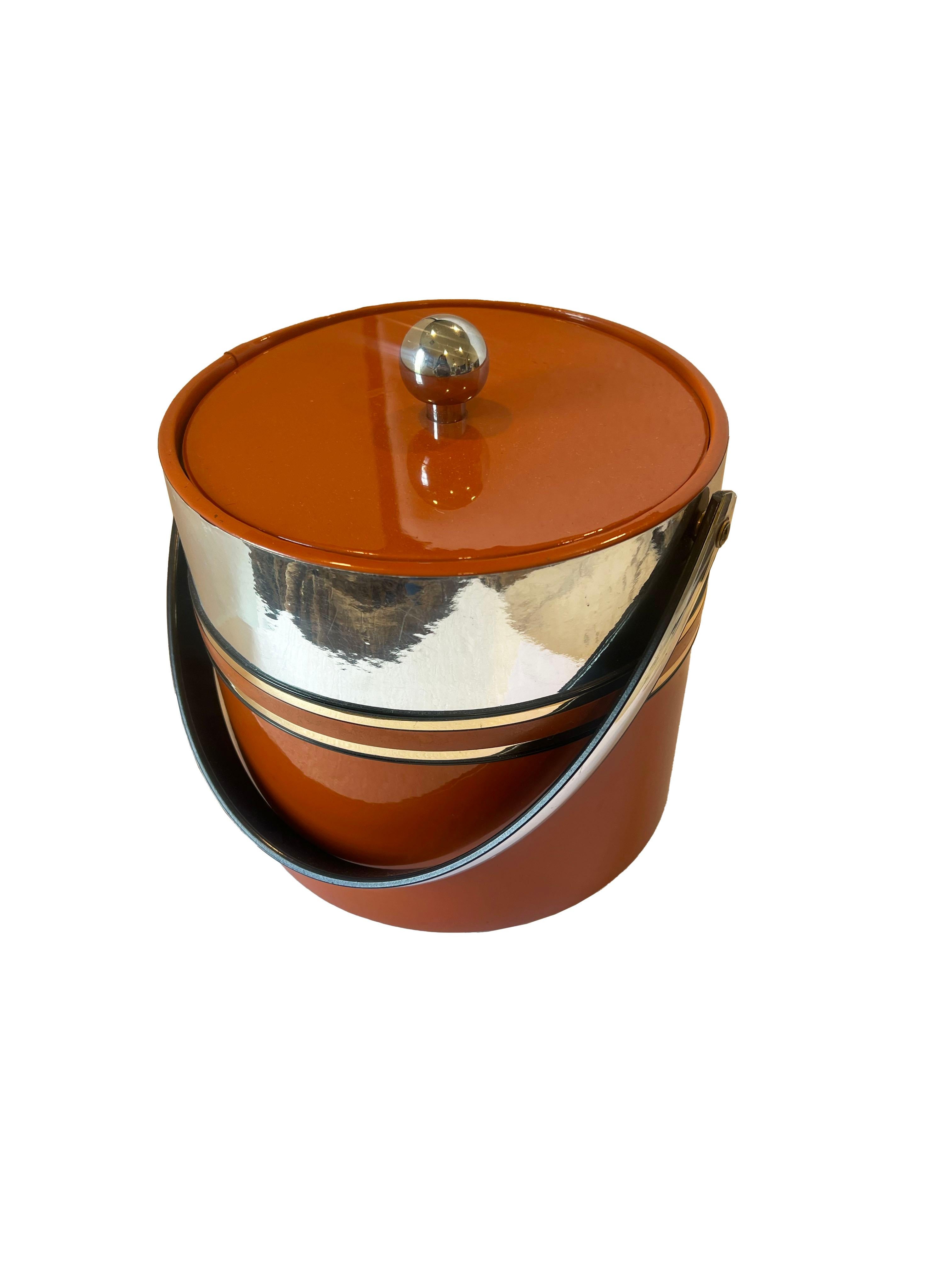 An exquisite vintage Hermes style ice bucket that combines aesthetic appeal & functionality. This piece boasts a vibrant orange color, infusing a pop of retro charm into any setting and is embellished with gold and silver accents. The addition of a