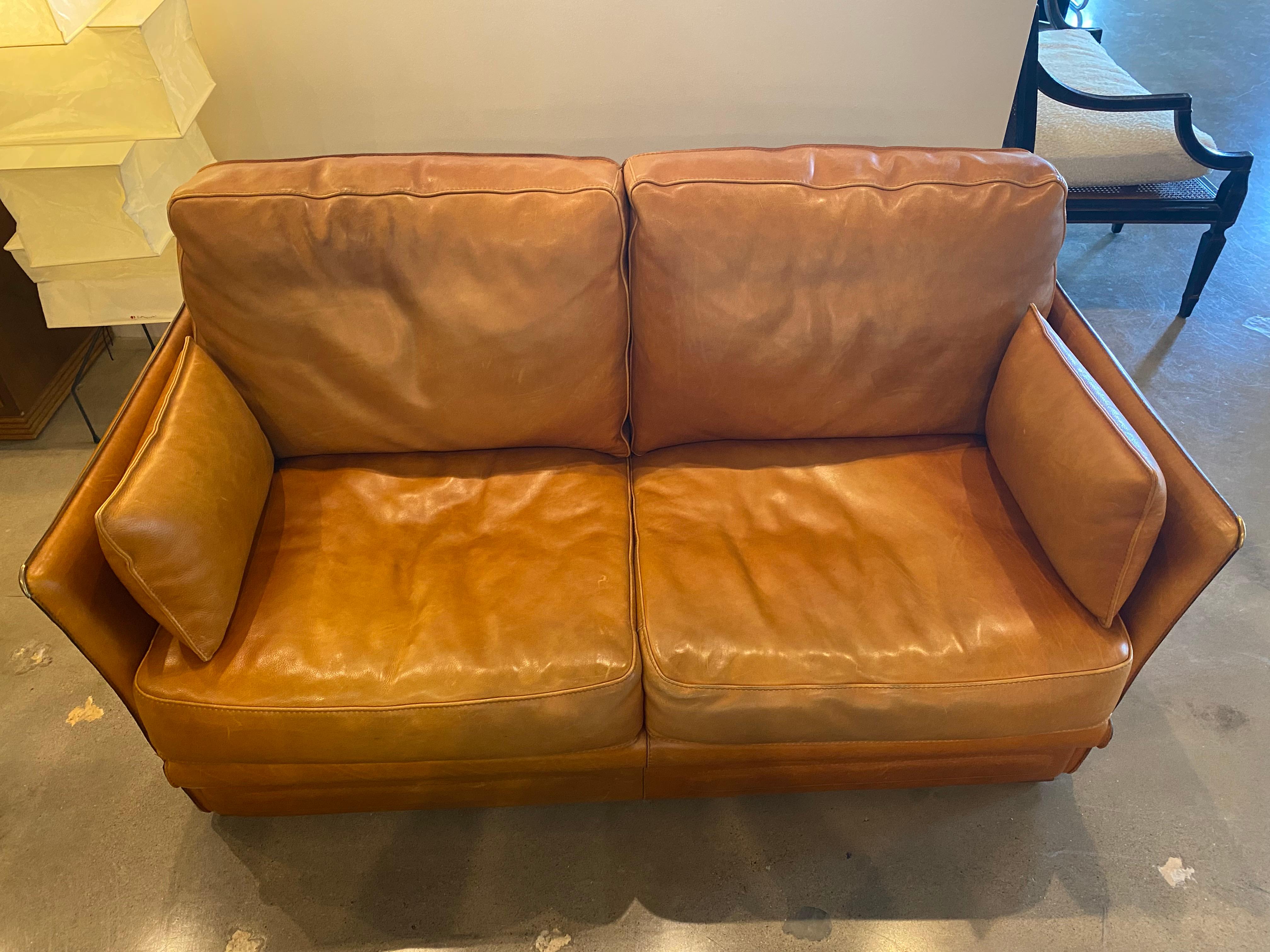 Hermes style loveseat in cognac leather with detailed seams and brass accents. Two matching pillows included with each sofa. Two available, sold separately. France, 1970-80.