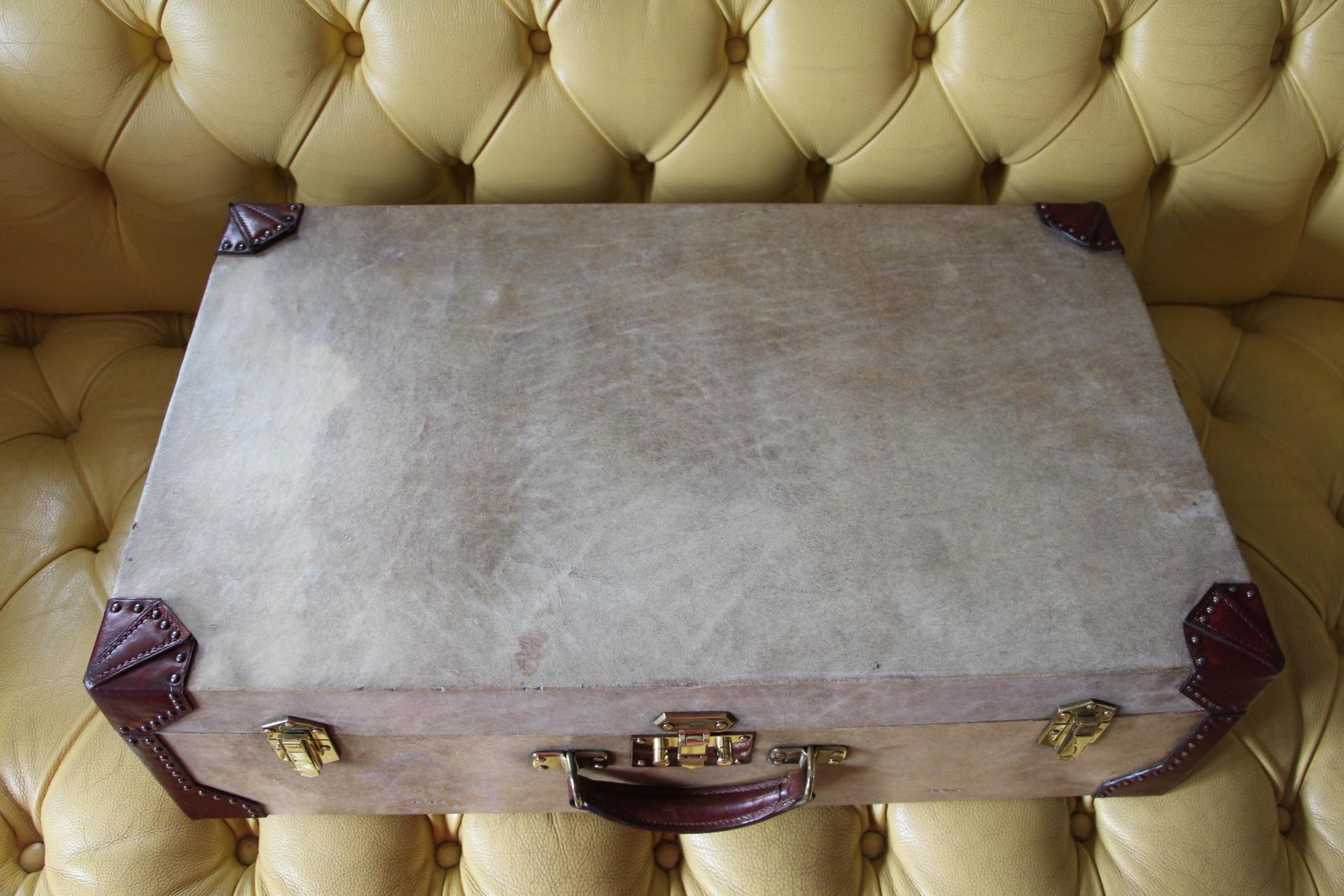 This very nice Hermès suitcase is in beige vellum and leather. Its corners as well as its handle are in this typical Hermès red leather. Its ivory color vellum is gently patinated and offers a kind of marbred look that adds a touch of charm and