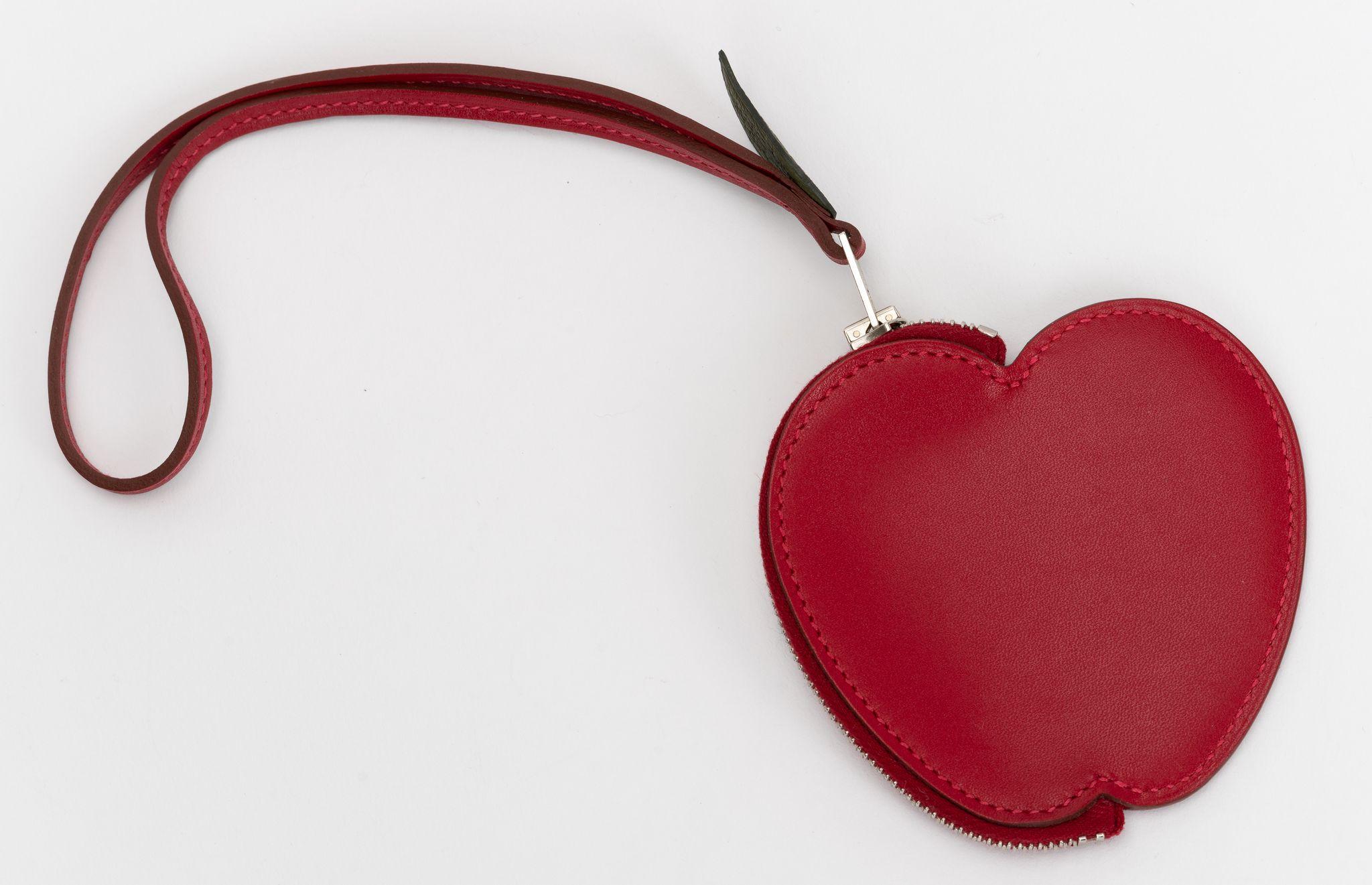 The Hermes Tadelakt Tutti Frutti Pomme Coin Purse Wristlet in Rouge Vif is a small bag charm also doubles as a wristlet coin purse. This apple shaped coin purse is is made from bright red calfskin, the zipper handle features a canopee green leaf