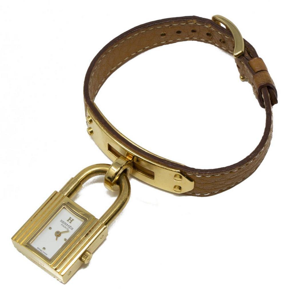 Iconic Hermes Kelly Watch with Gold Hardware in Tan Leather. Watch is stamped in corner with a circle “X”, indicative of the Hermes 1994 date. Serial number 671037 on bottom underside of lock. Lock-formed with white dial marked “Hermes Paris” and