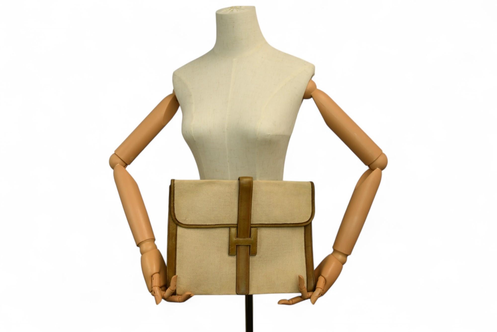 This timeless Hermès Jige clutch features a structured envelope silhouette crafted in signature beige toile canvas with luxurious tan Peau Porc (pigskin) leather trim. Known for its fine grain and soft sheen, Peau Porc adds refined texture to the