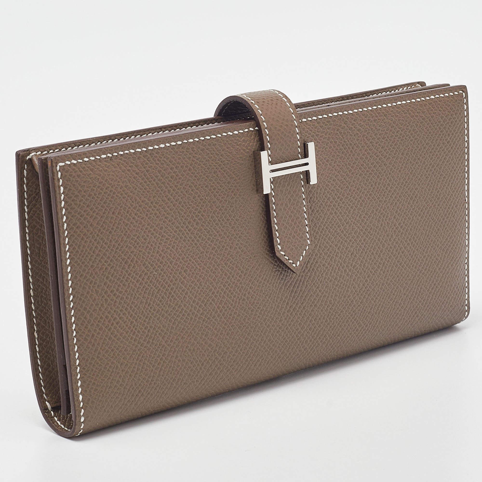 The Hermès Bearn wallet showcases exquisite craftsmanship. The supple Epsom leather in a sophisticated taupe hue is complemented by a sleek palladium-finished H logo closure. Inside, well-organized compartments and card slots offer both style and