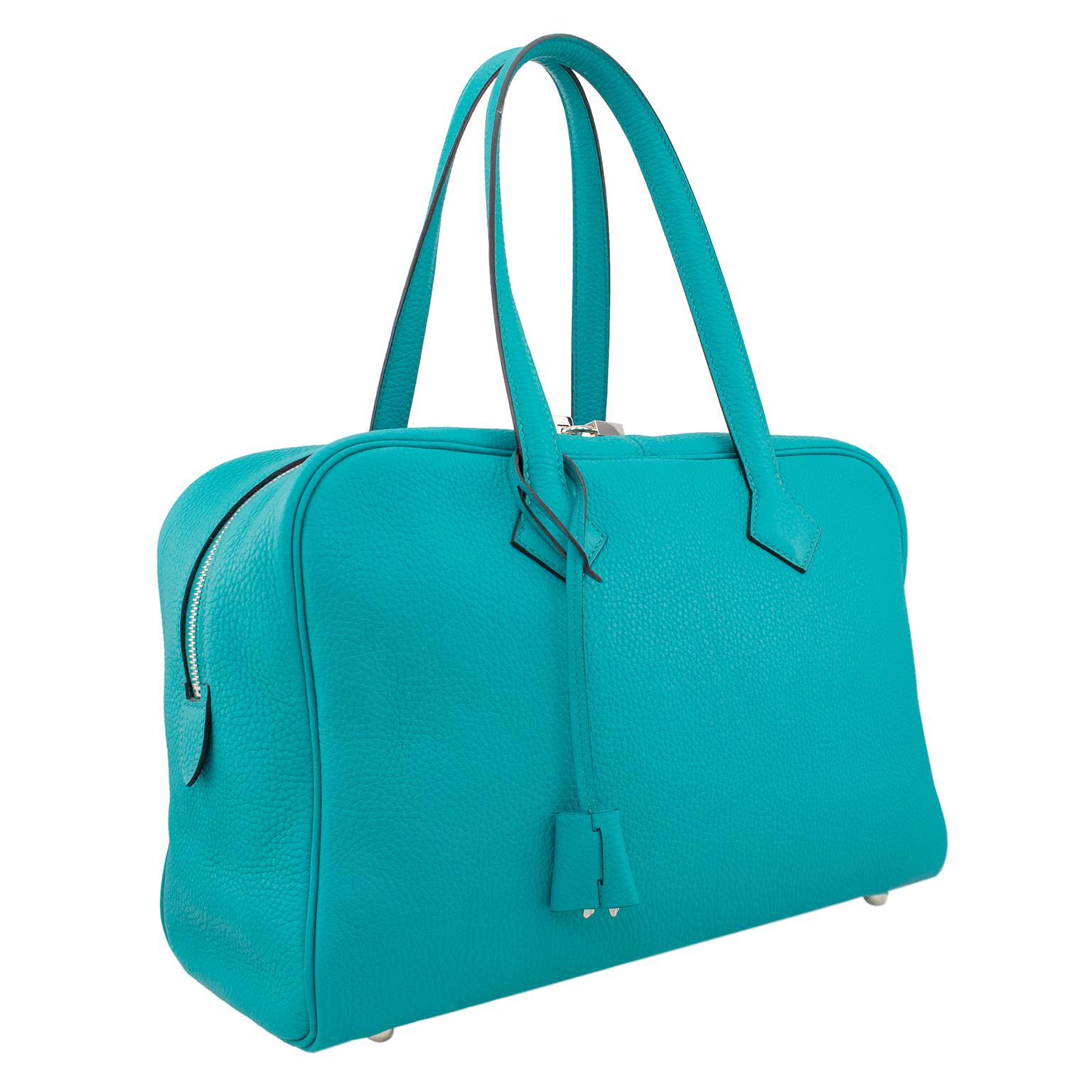 Authentic Hermes Taurillon Clemence Novillo Victoria II 35 in turquoise. It features very tall leather strap handles, a double palladium zipper with lock and opens to a beige herringbone fabric interior with zippered and patch pockets. Taurillion