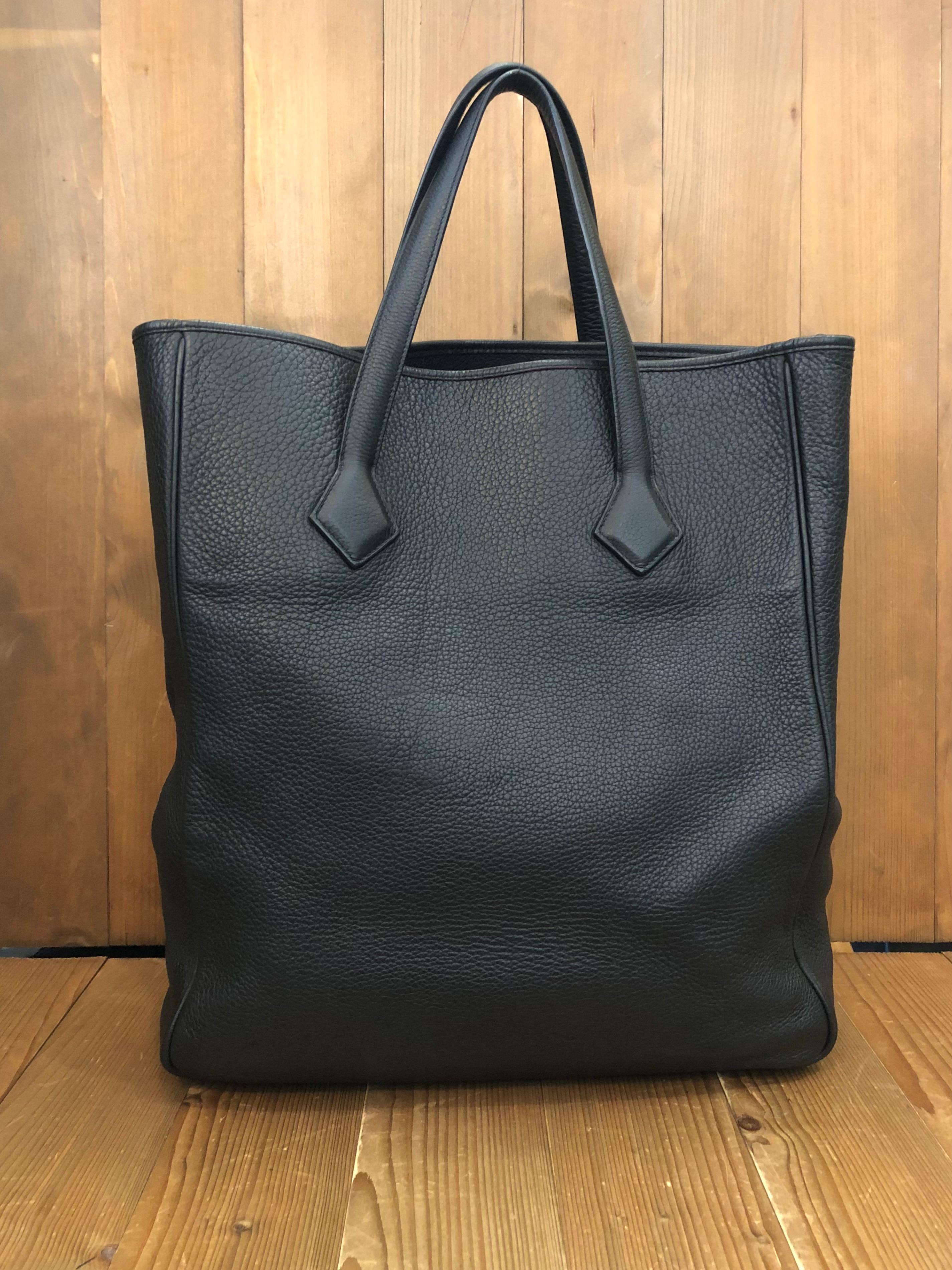 This stylish Hermes tote is crafted of taurillion clemence calfskin leather in black. This tote features two long leather straps for carrying on your shoulder comfortably. Wide top opens to a leather interior featuring a zippered pocket. This