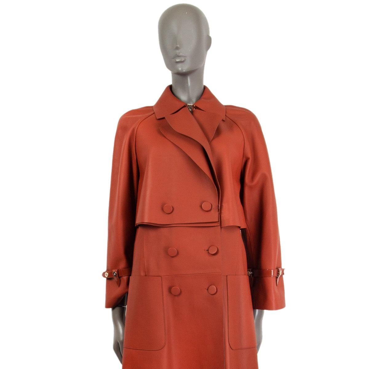 authentic Fendi double-breasted trench coat in terra cotta lamb leather with a peak collar and deep slip frontal pockets. Closes with buttons and fastens with one hook at the neckline. Has long sleeves with patent leather band details. Lined in