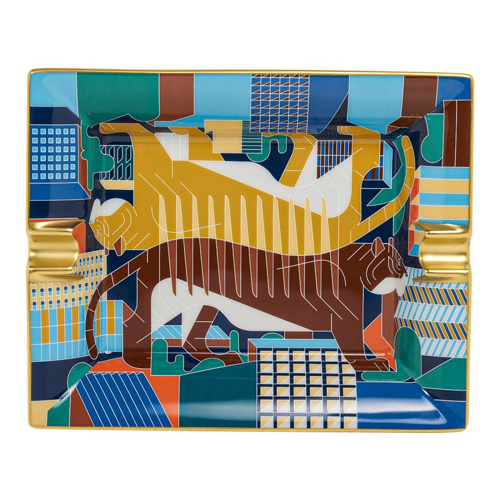 Mightychic offers an Hermes Tigre en Miroir  Limoges porcelain ashtray.
Depicts mirror images of a tiger walking about the city.
Beautiful rich cool colours accented with warm hues.
Hand painted gold trim and decorated using chromolithography.
A