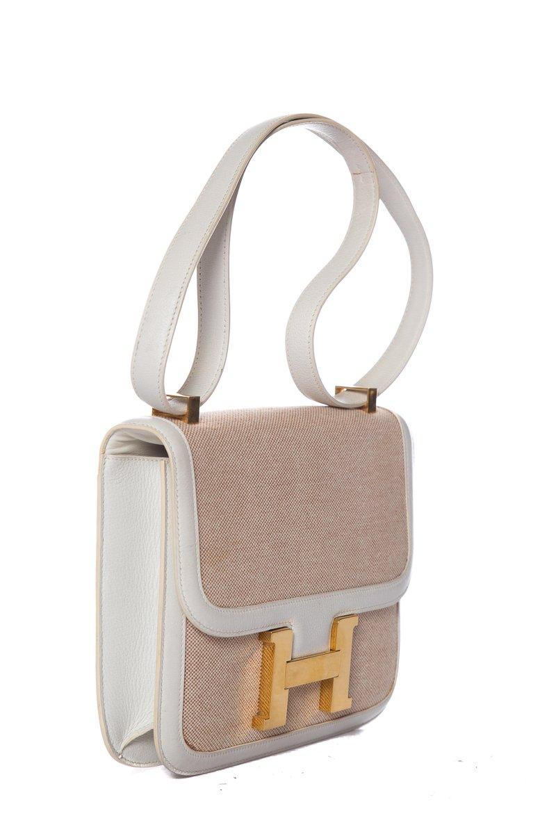 Hermès Constance Toile tan toile gold hardware. The Constance by Hermès is one of the house's most iconic designs. The understated chicness of this compact box bag presents itself in the distinctive gold-toned H buckle, and cream leather trim.