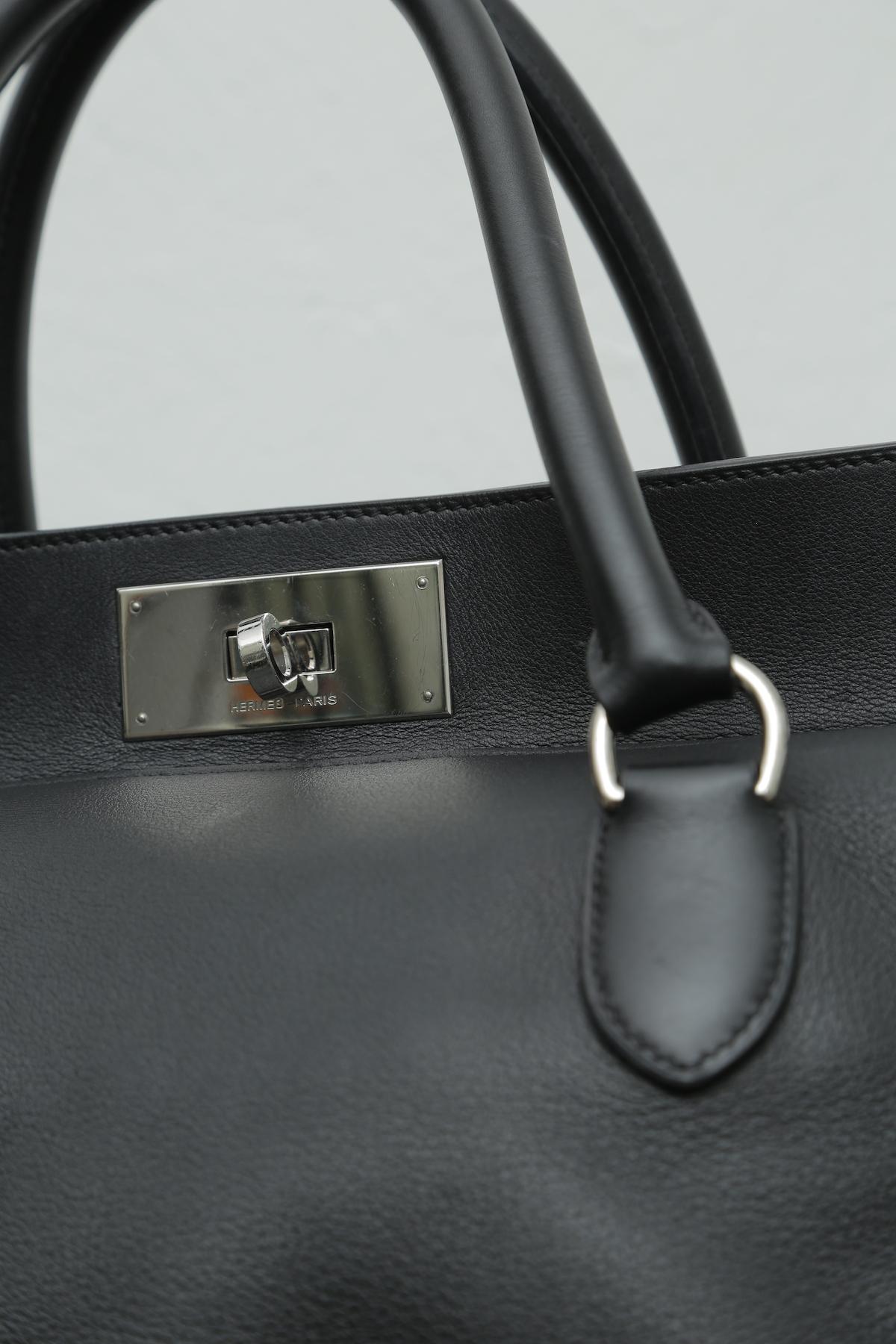 
Hermes black toolbox 33 with silver hardware and detachable shoulder strap. This bag features dual rolled top handles, soft frame top and palladium tone hardware. Its turn lock closure opens to a beige fabric interior with patch pockets. This bag