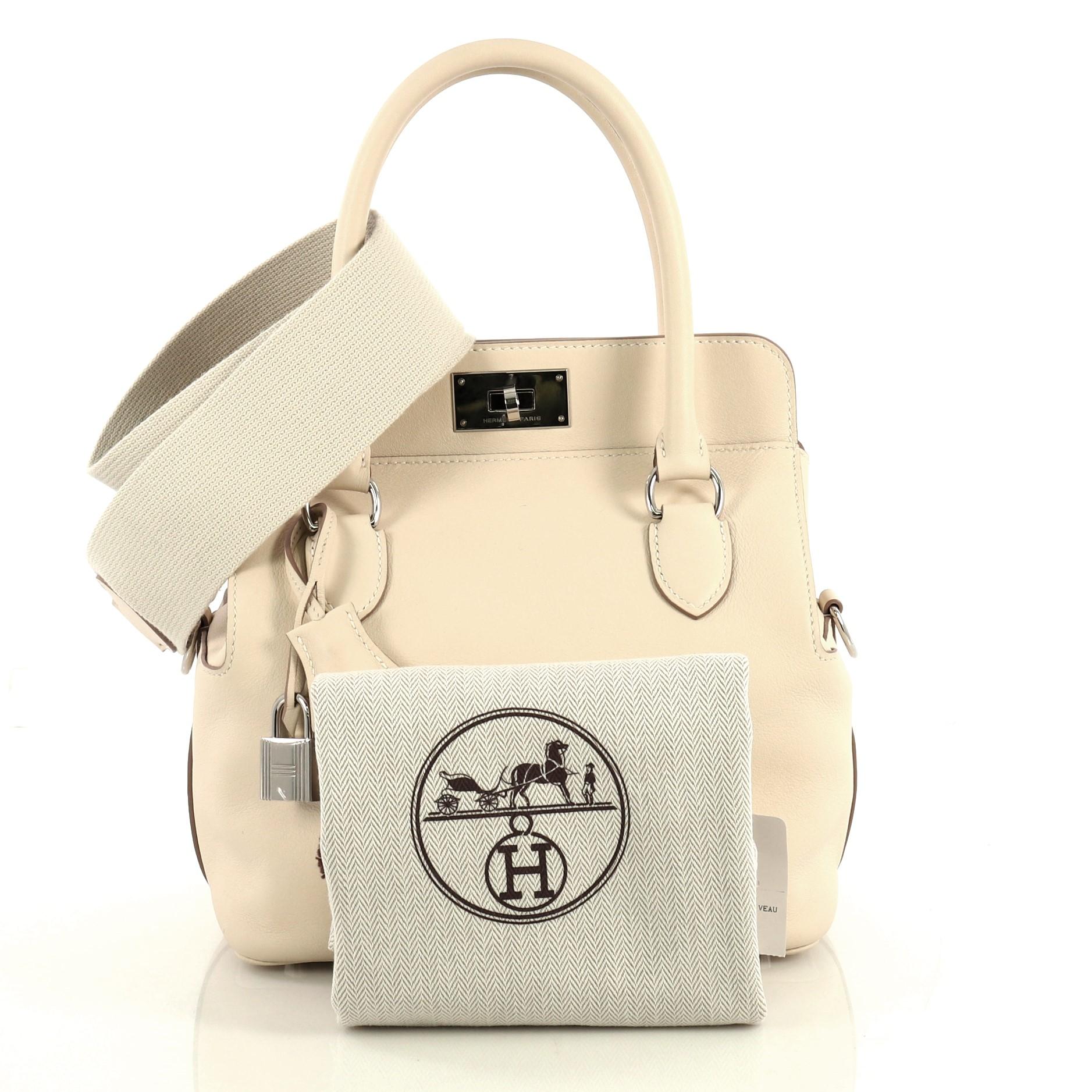 This Hermes Toolbox Handbag Swift 20, crafted from Craie neutral Swift leather, features dual rolled top handles, soft framed top, and palladium hardware. Its turn-lock closure opens to a Craie neutral Swift leather interior with slip pockets. Date