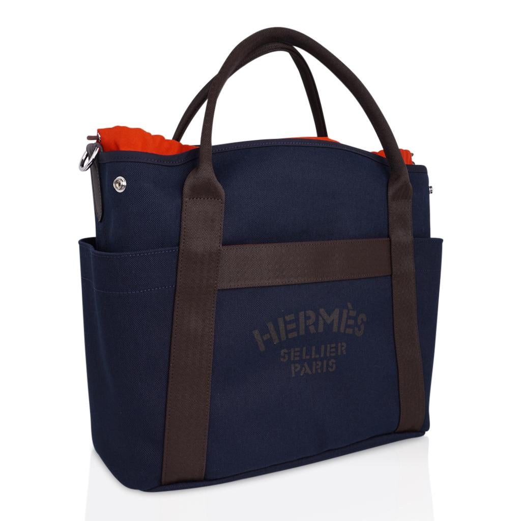Guaranteed authentic Hermes Sac De Pansage Grooming Bag tote features Bleu Navy canvas with Feu interior and Palladium hardware. 
Hermes Sellier Paris printed on the front.
This versatile tote bag has brown handles, trim and brown shoulder